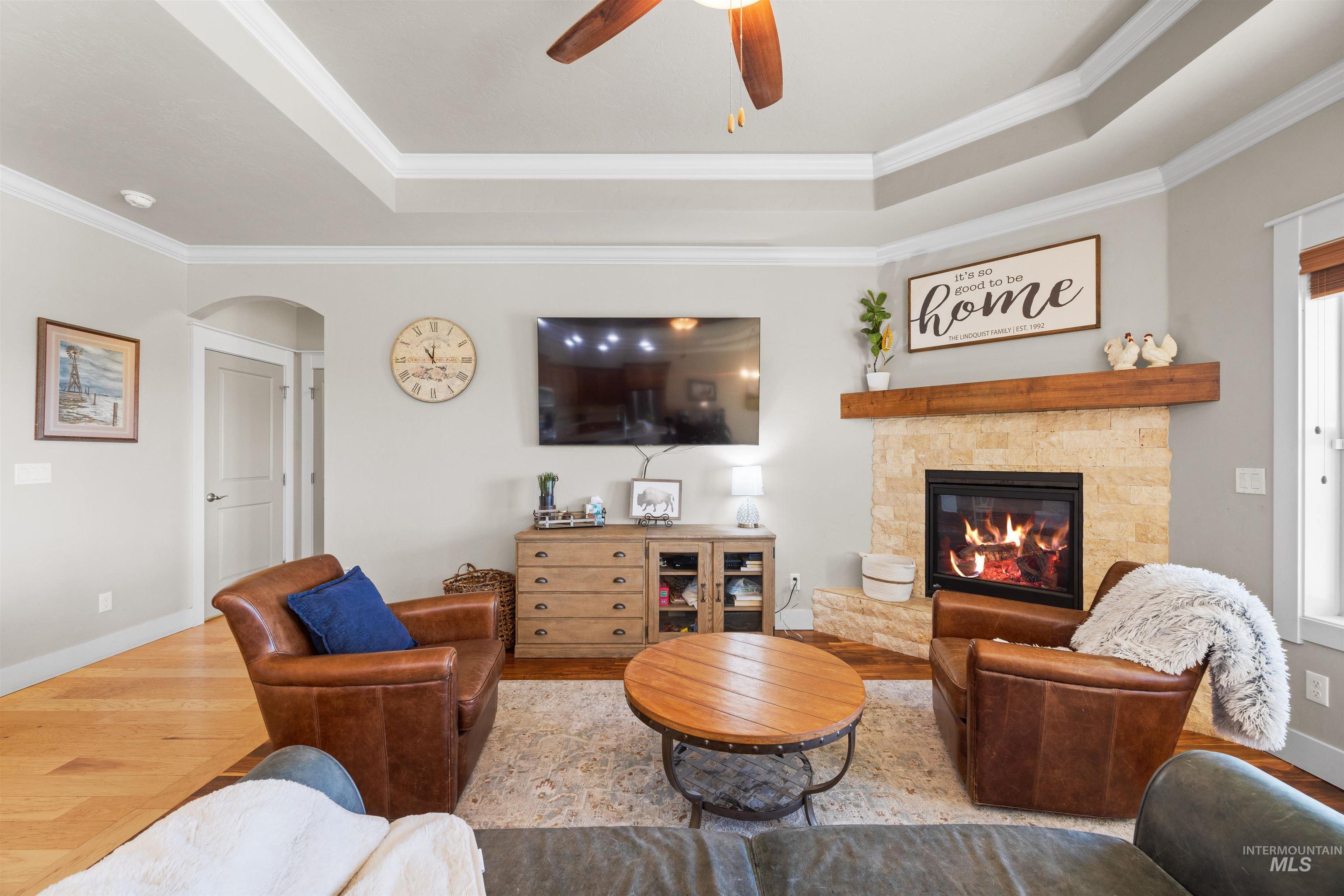 Living room with a raised ceiling, wood finished floors, a fireplace, and ornamental molding