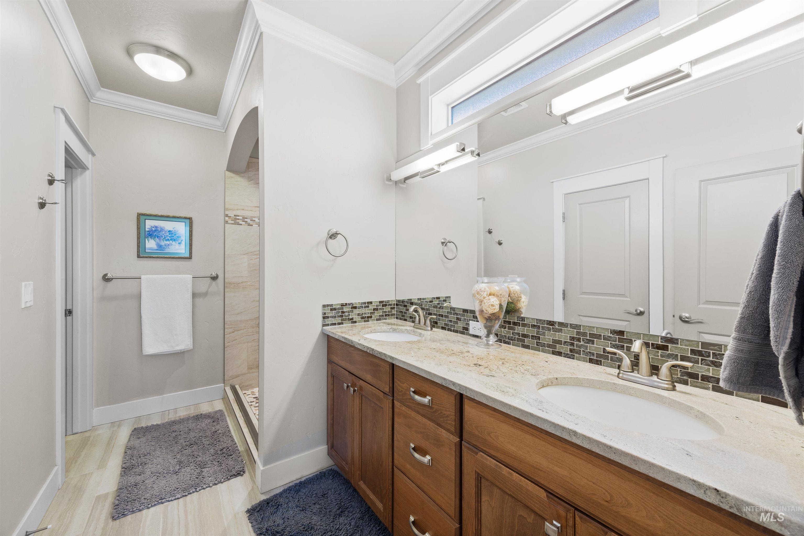 Bathroom featuring crown molding, double vanity, a shower stall, backsplash, and light wood-type flooring