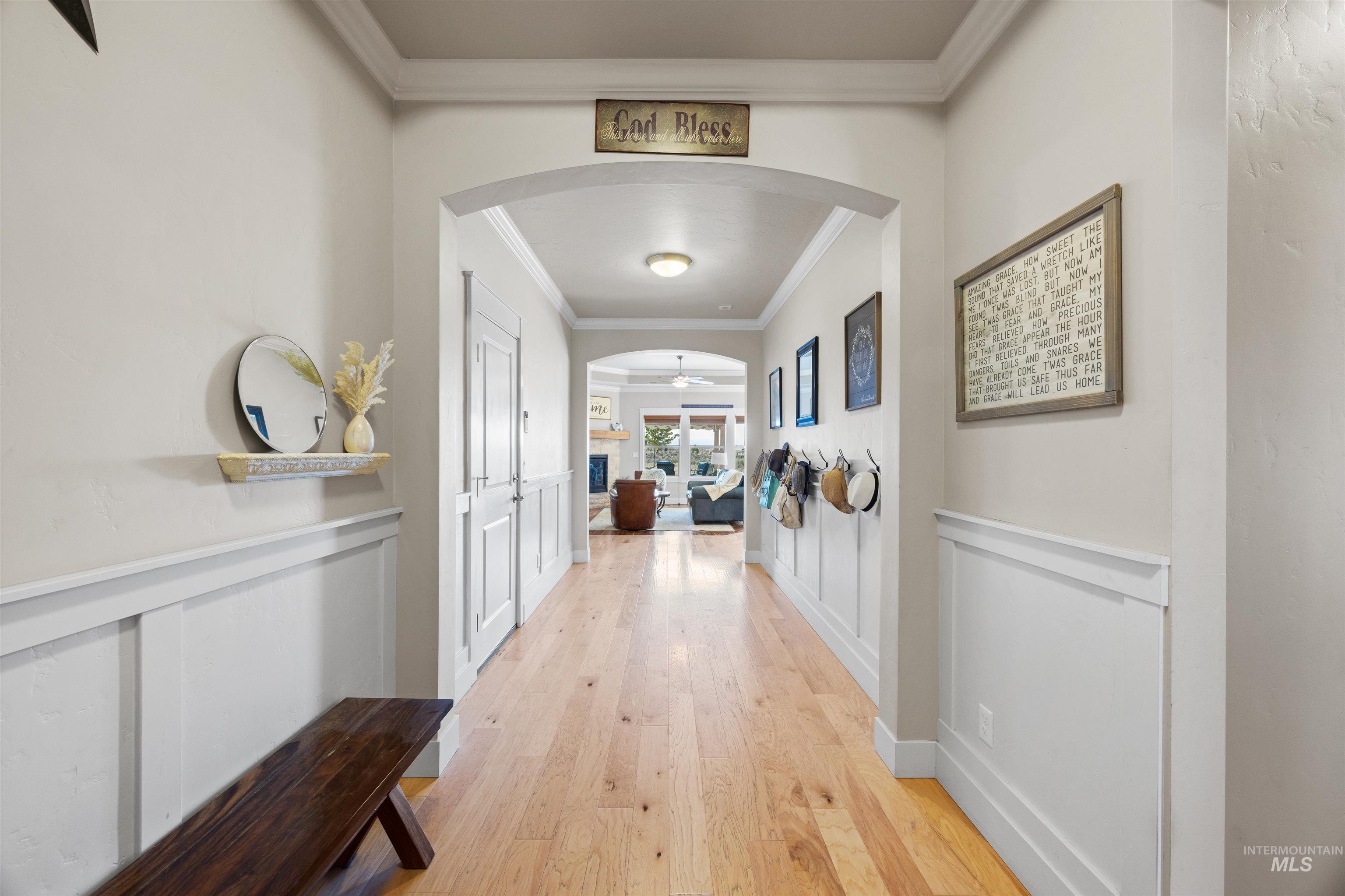 Hallway with light wood-type flooring, arched walkways, ornamental molding, a decorative wall, and wainscoting