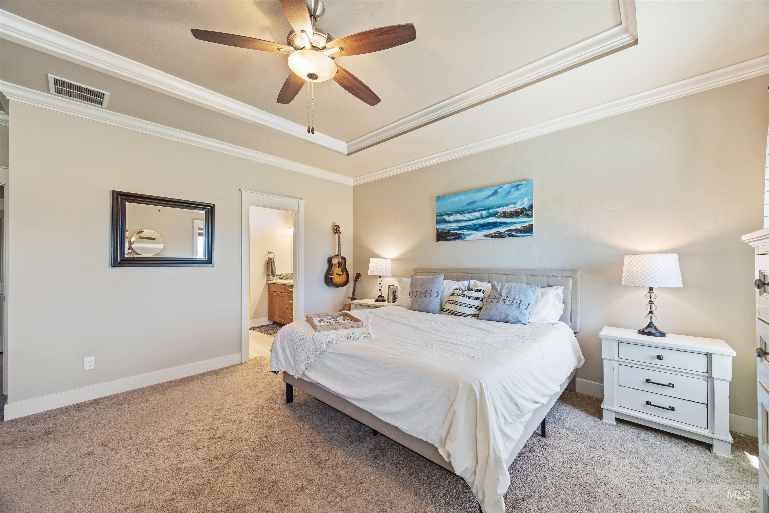 Bedroom with ornamental molding, light colored carpet, a ceiling fan, connected bathroom, and a tray ceiling