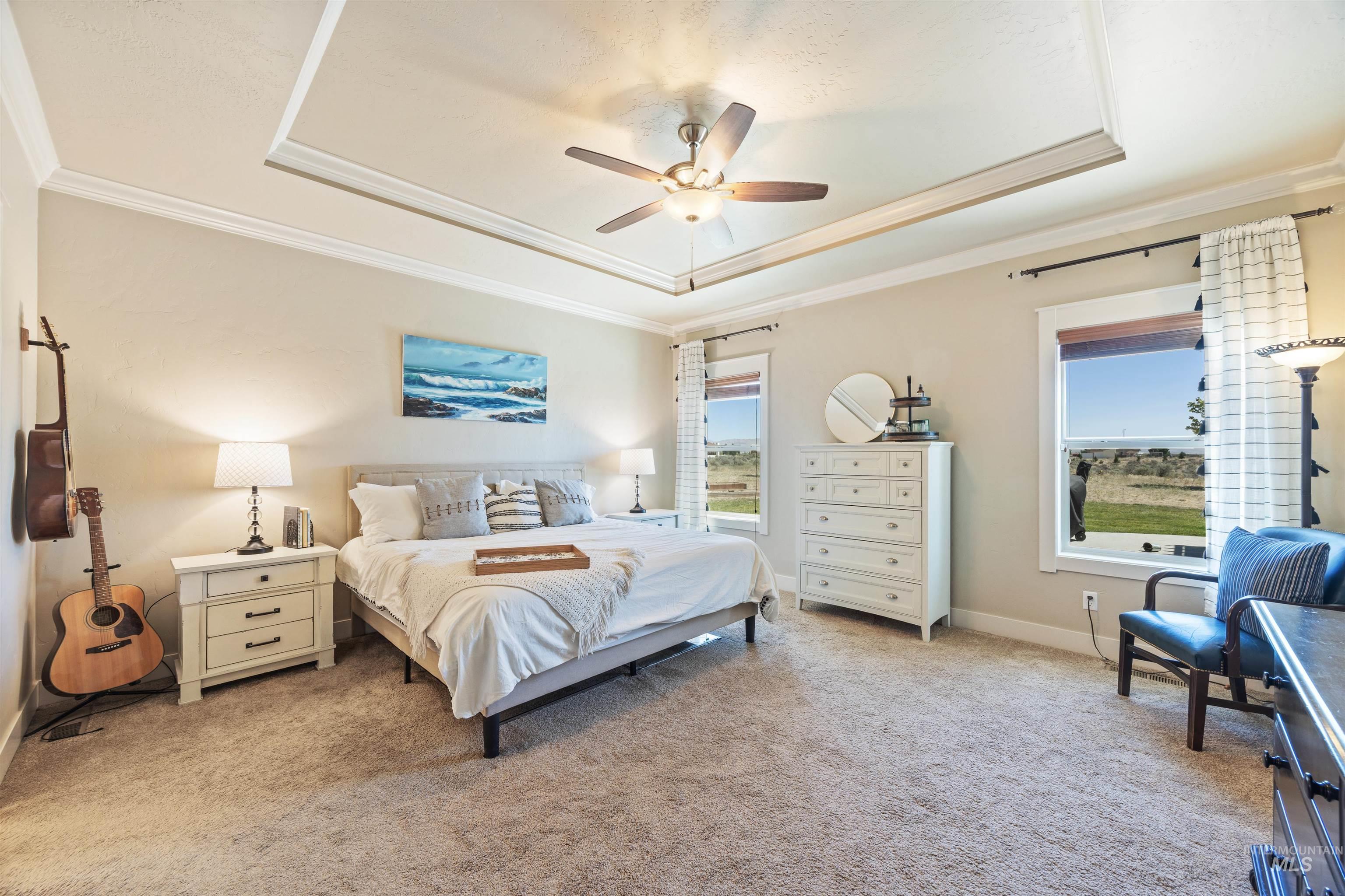 Bedroom with a tray ceiling, ornamental molding, light colored carpet, and ceiling fan