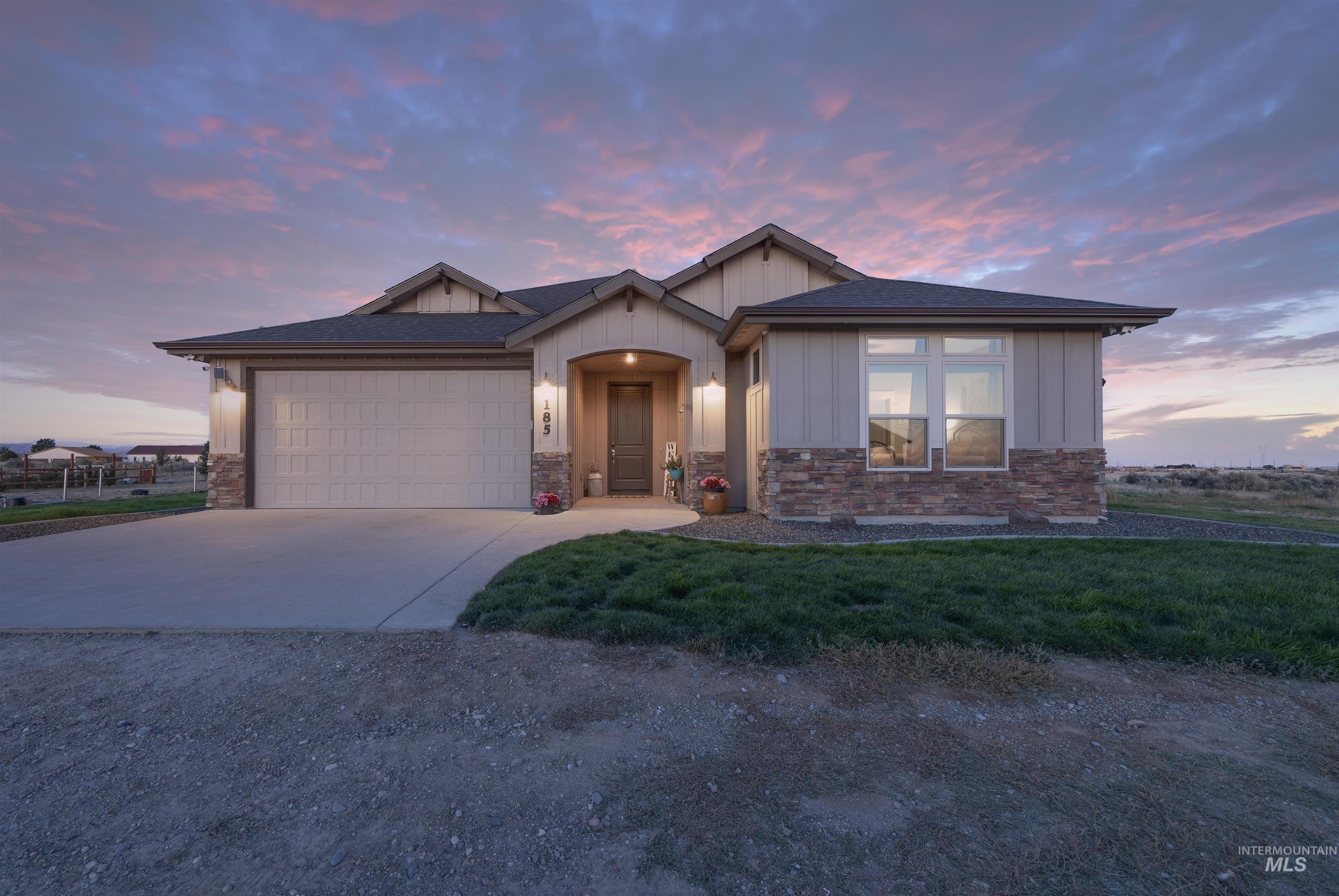 View of front of property featuring driveway, stone siding, an attached garage, and board and batten siding