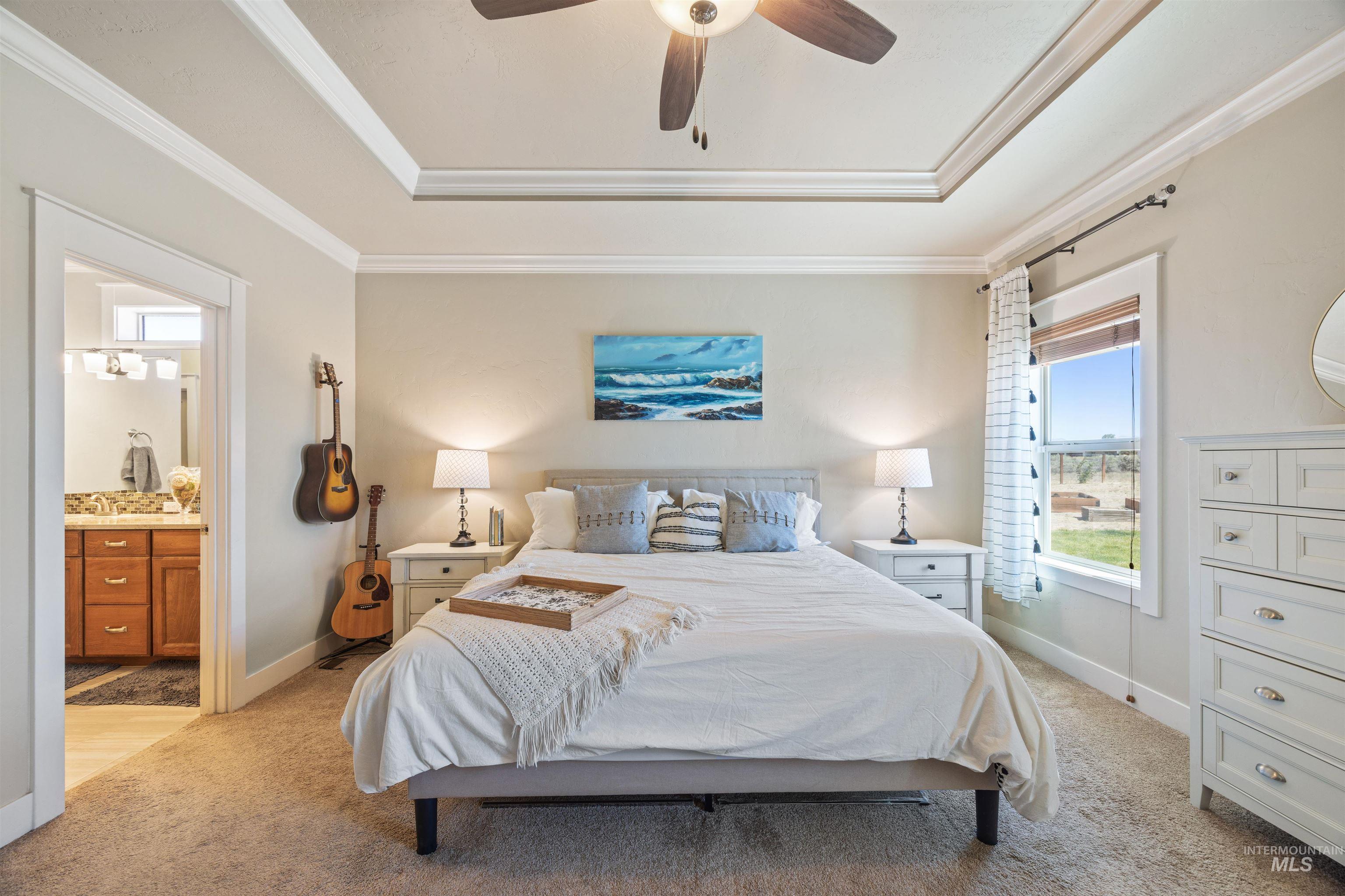 Bedroom with light carpet, a raised ceiling, a ceiling fan, ornamental molding, and ensuite bath
