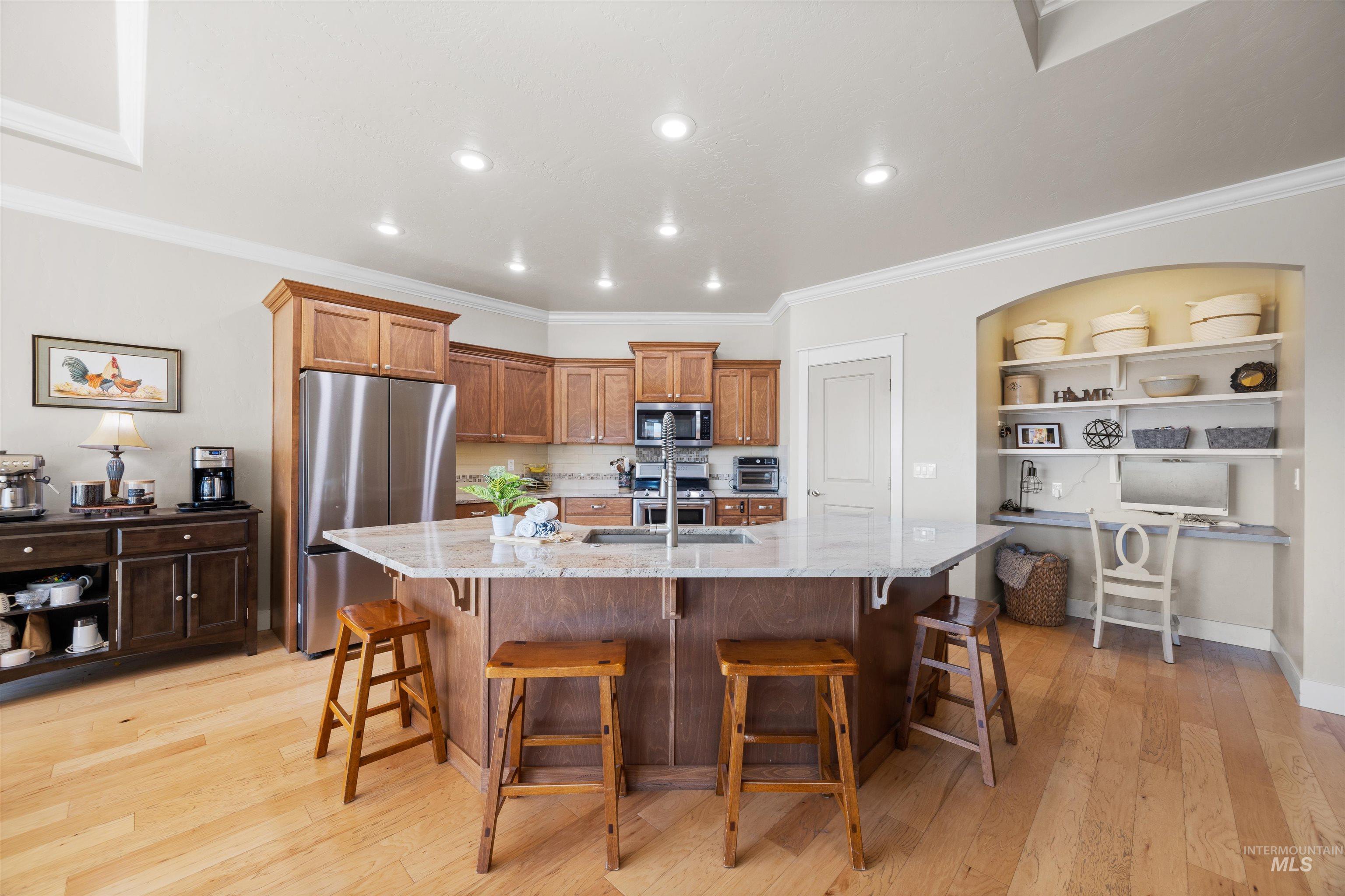 Kitchen featuring a breakfast bar, brown cabinetry, stainless steel appliances, crown molding, and light stone counters