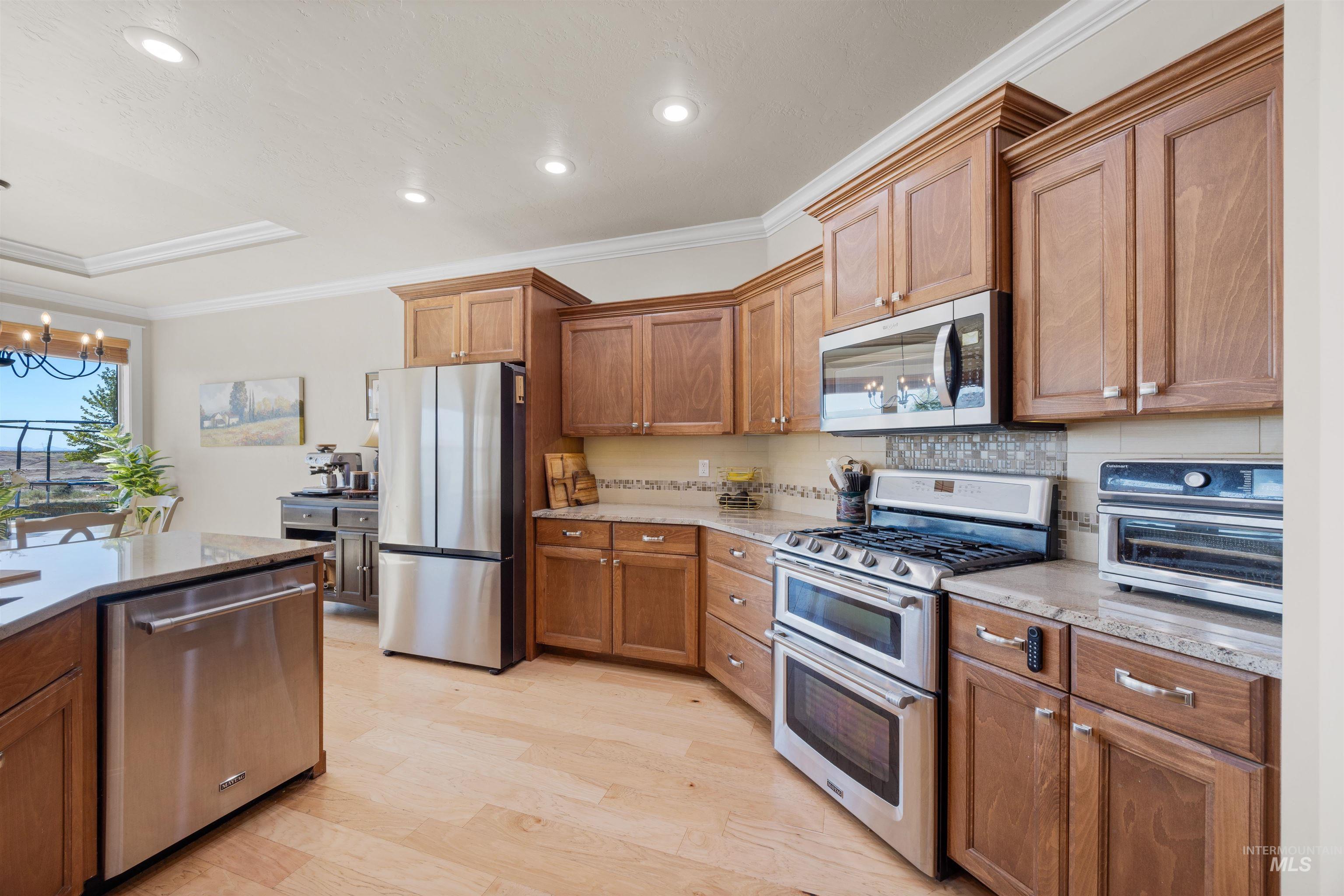 Kitchen featuring ornamental molding, stainless steel appliances, brown cabinetry, decorative backsplash, and light wood finished floors
