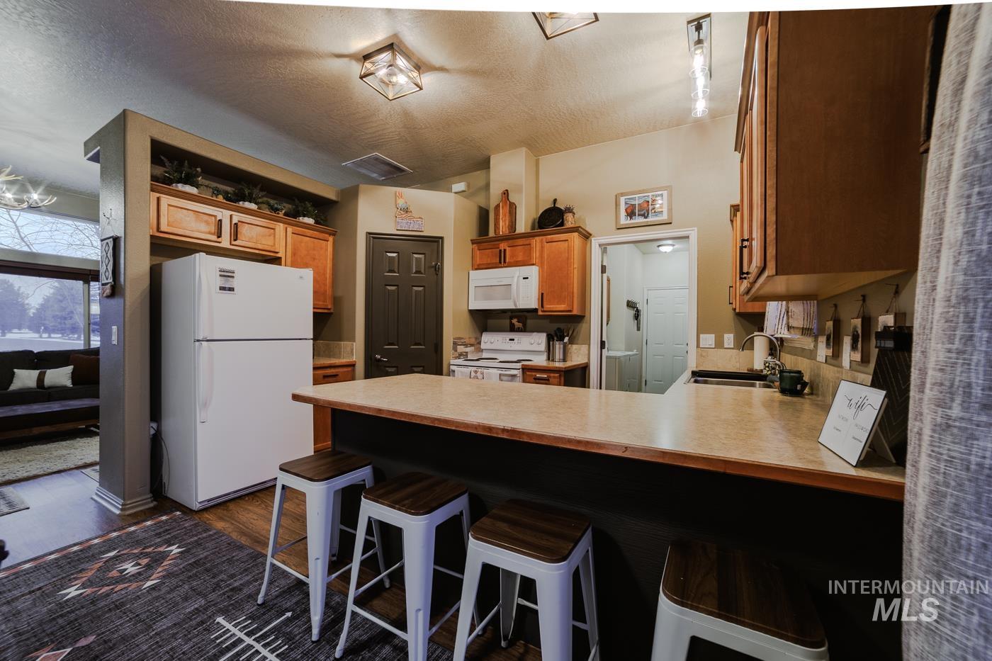 Kitchen featuring a breakfast bar, white appliances, a peninsula, light countertops, and dark wood-style flooring