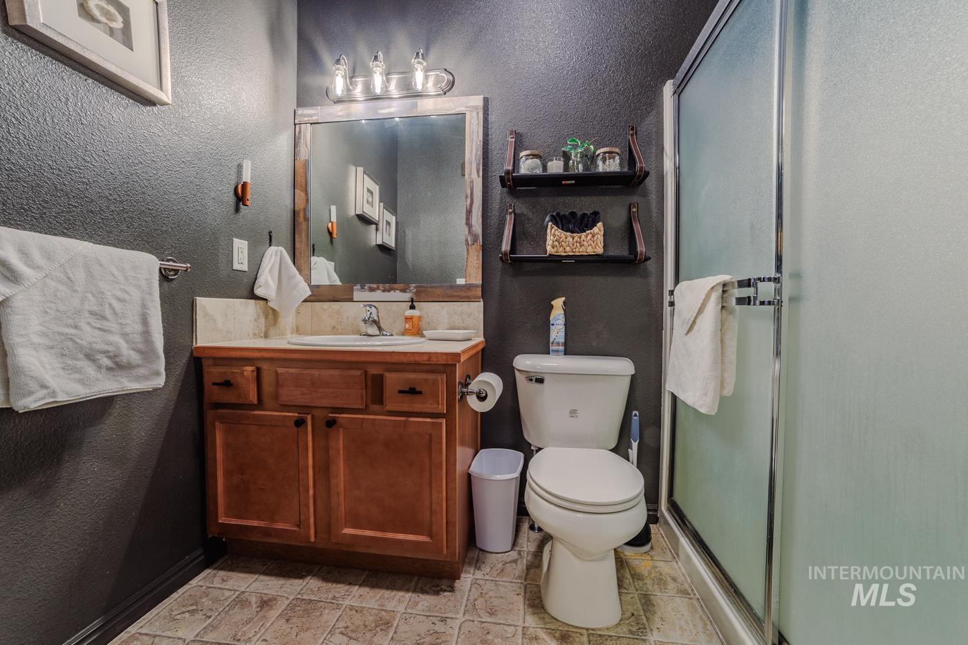 Bathroom with a textured wall, vanity, and a shower stall