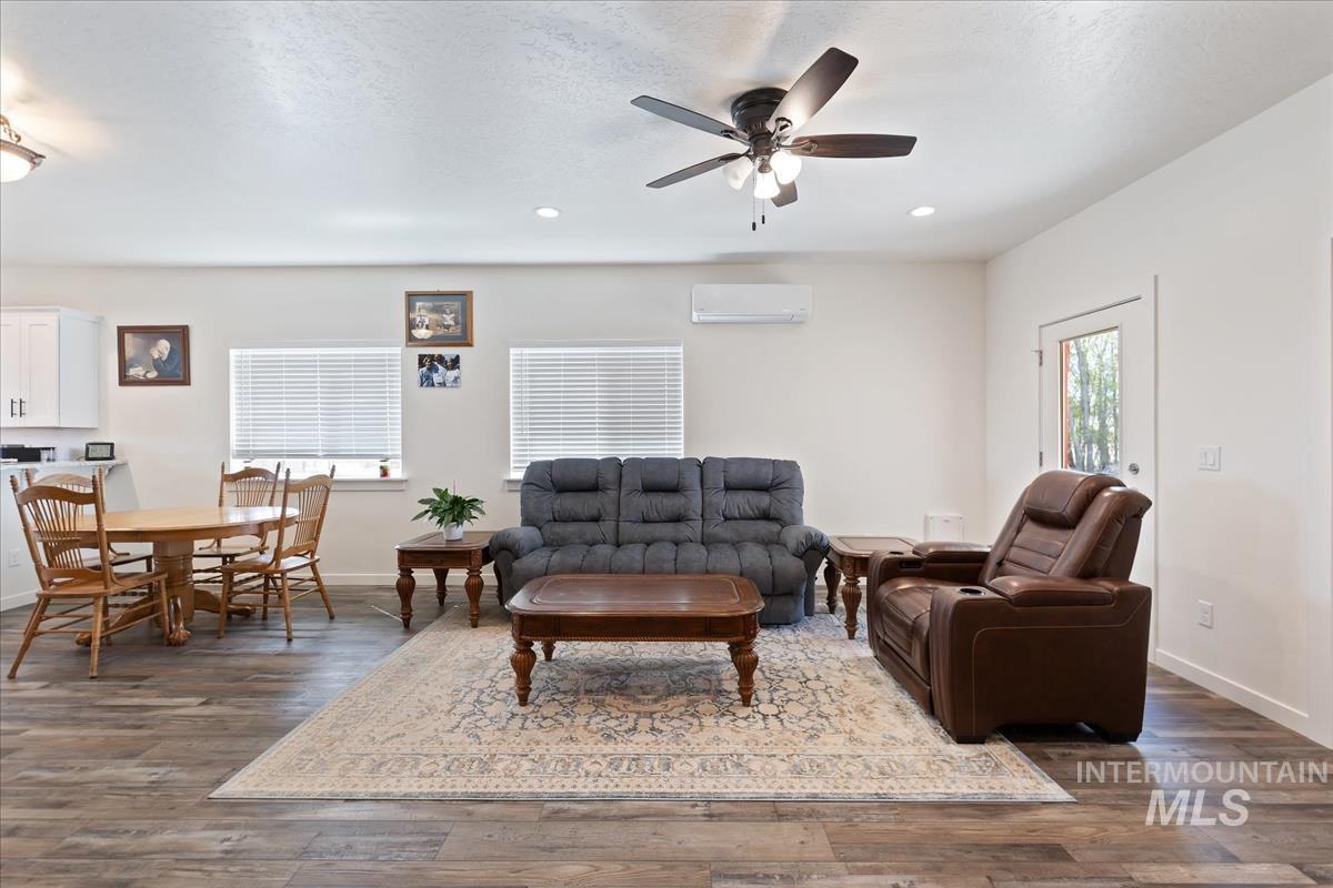 Living room featuring a ceiling fan, dark wood-type flooring, a wall unit AC, recessed lighting, and a textured ceiling