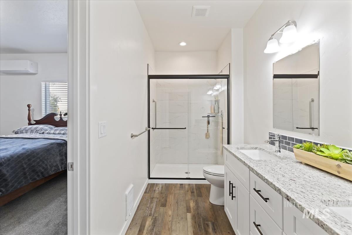 Ensuite bathroom with double vanity, a shower stall, a wall mounted air conditioner, dark wood-type flooring, and recessed lighting