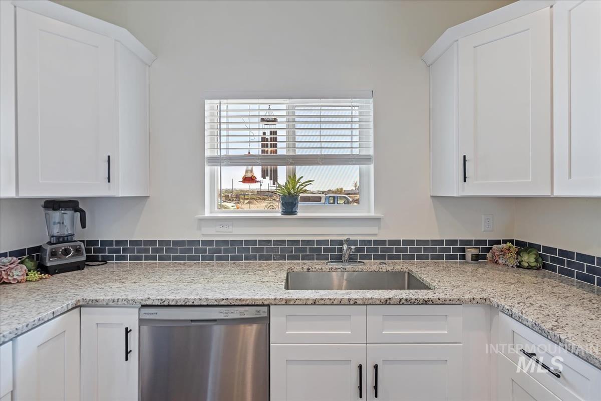 Kitchen featuring stainless steel dishwasher, white cabinets, and light stone countertops