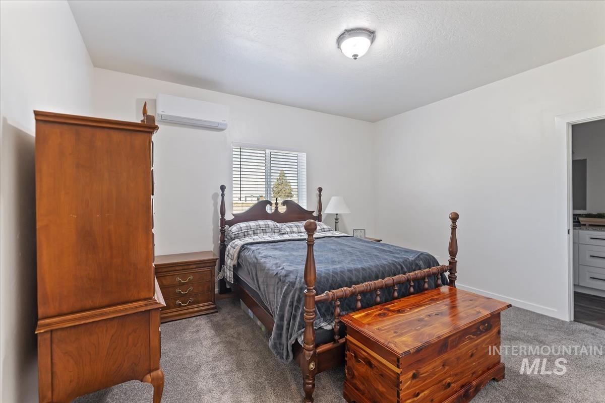 Bedroom featuring dark carpet, a wall mounted AC, a textured ceiling, and ensuite bath
