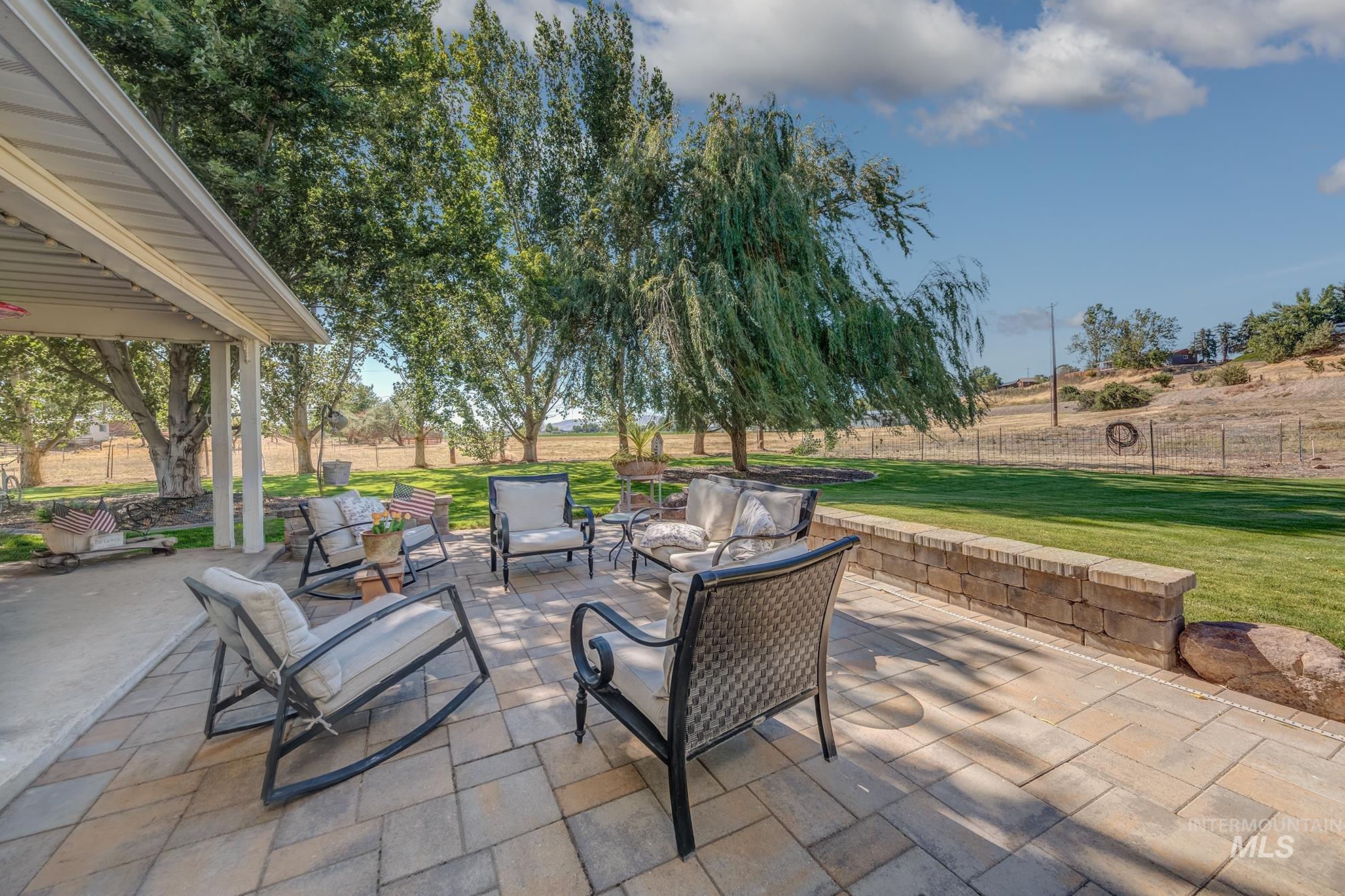 Expansive paver patio with a stone retaining wall, bordering a large grassy area
