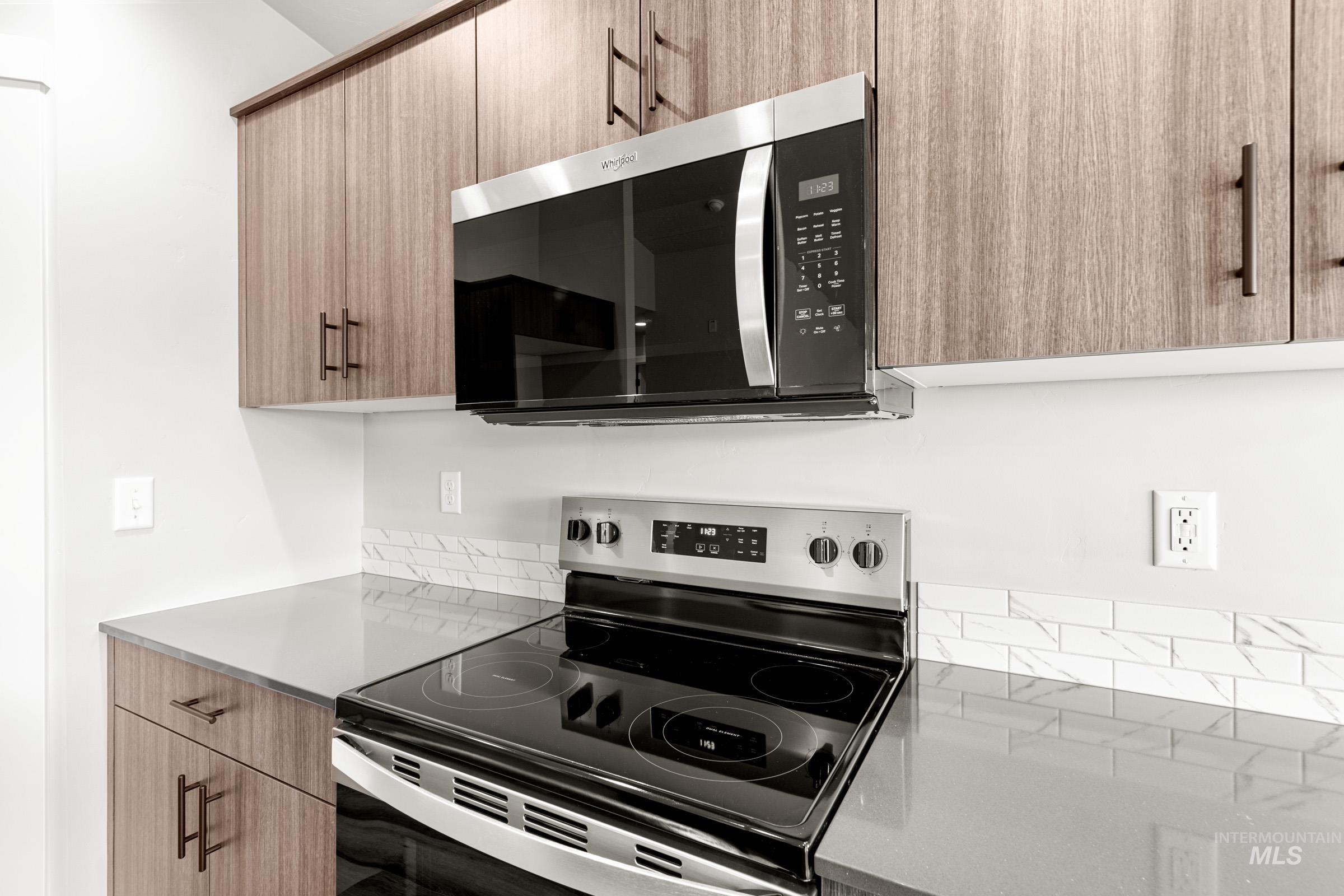 Kitchen featuring stainless steel appliances, modern cabinets, light stone counters, and light wood finish cabinetry