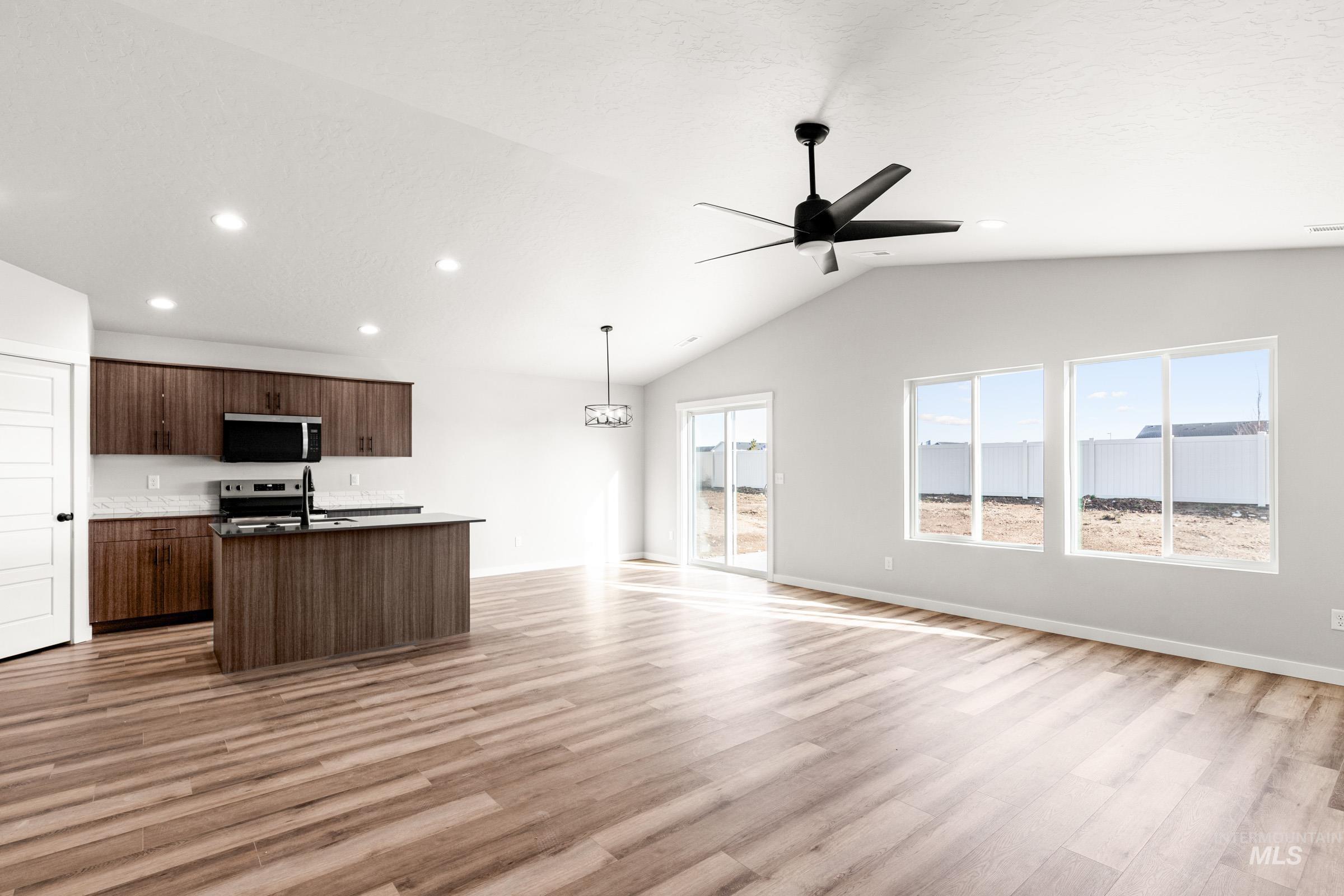 Kitchen with open floor plan, a center island with sink, stainless steel appliances, vaulted ceiling, and light wood-type flooring