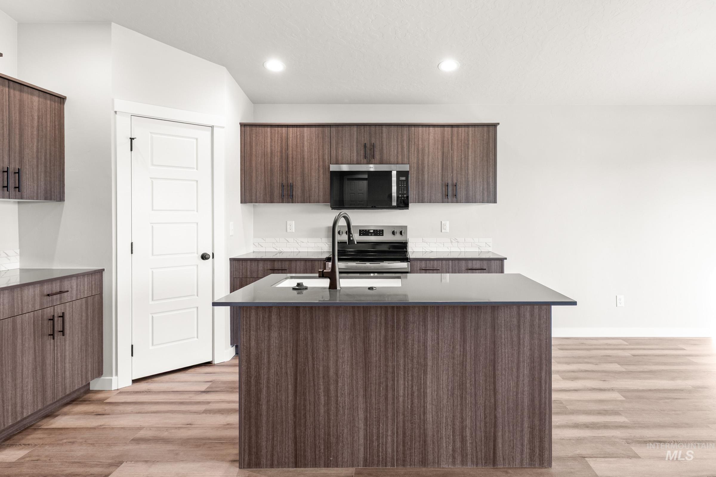 Kitchen with stainless steel appliances, light wood-style flooring, a kitchen island with sink, dark wood finish cabinets, and recessed lighting