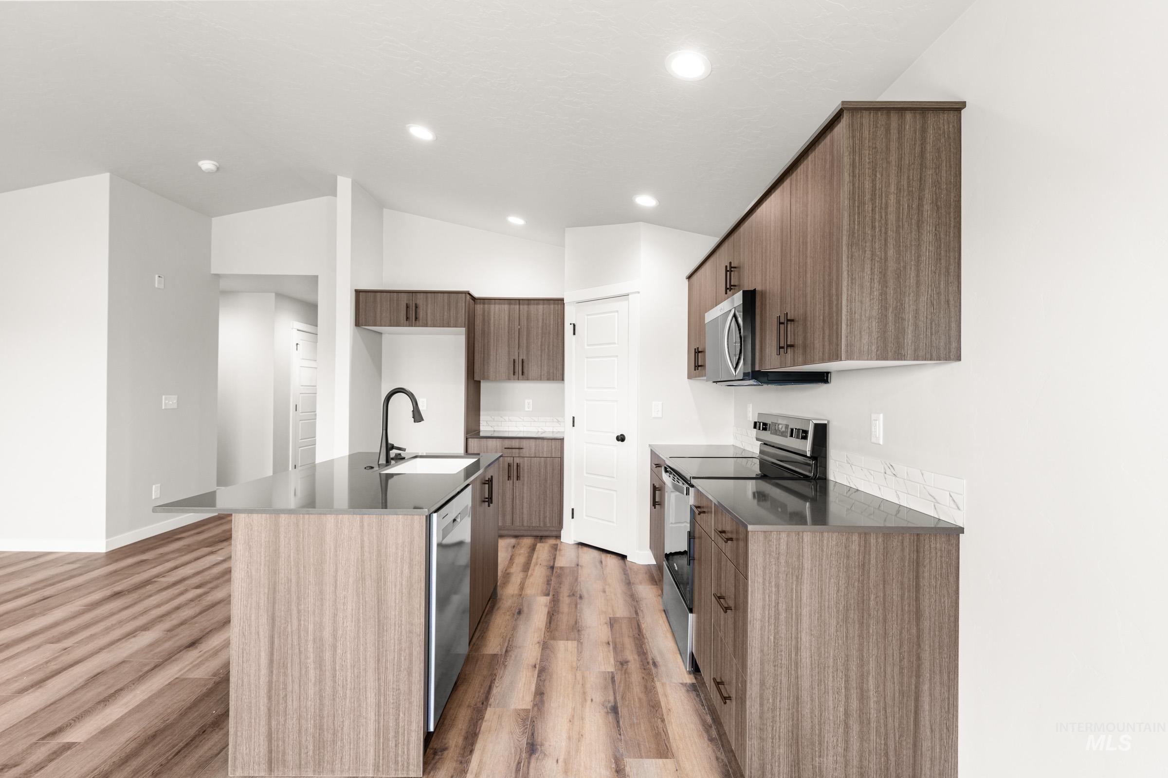 Kitchen with stainless steel appliances, modern cabinets, a kitchen island with sink, light wood-type flooring, and dark stone counters
