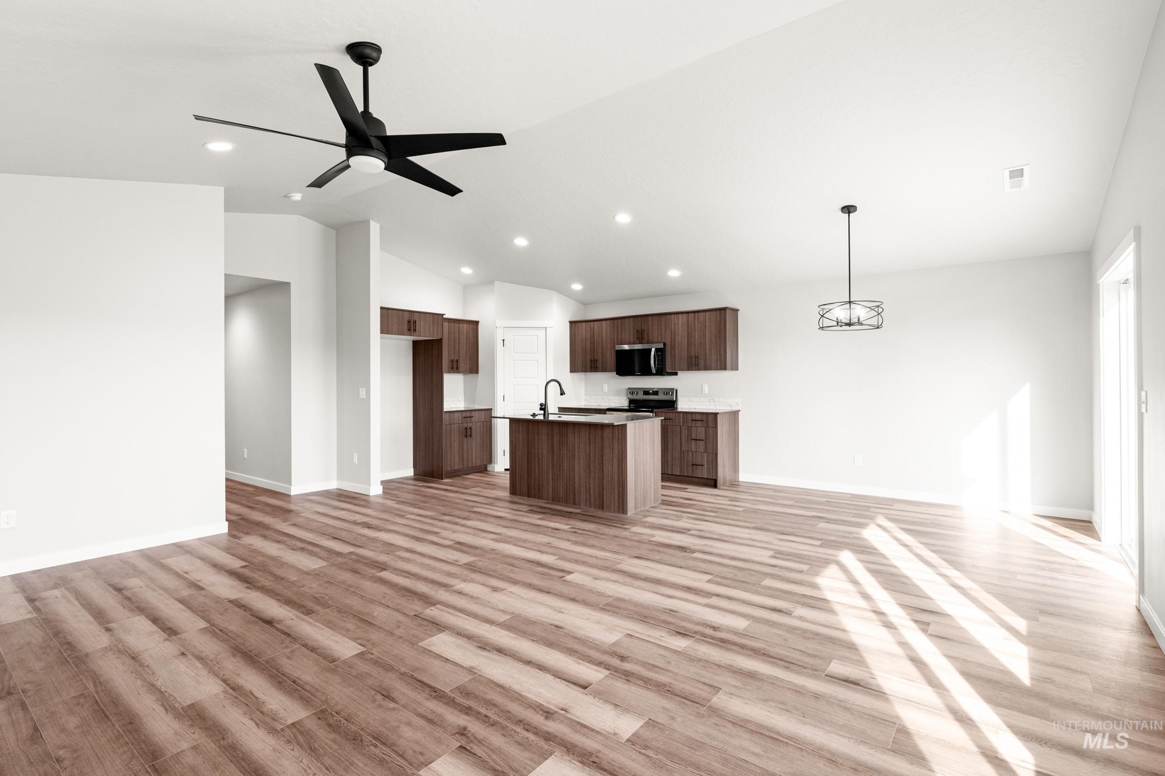 Kitchen with open floor plan, a ceiling fan, a center island with sink, vaulted ceiling, and light wood-type flooring