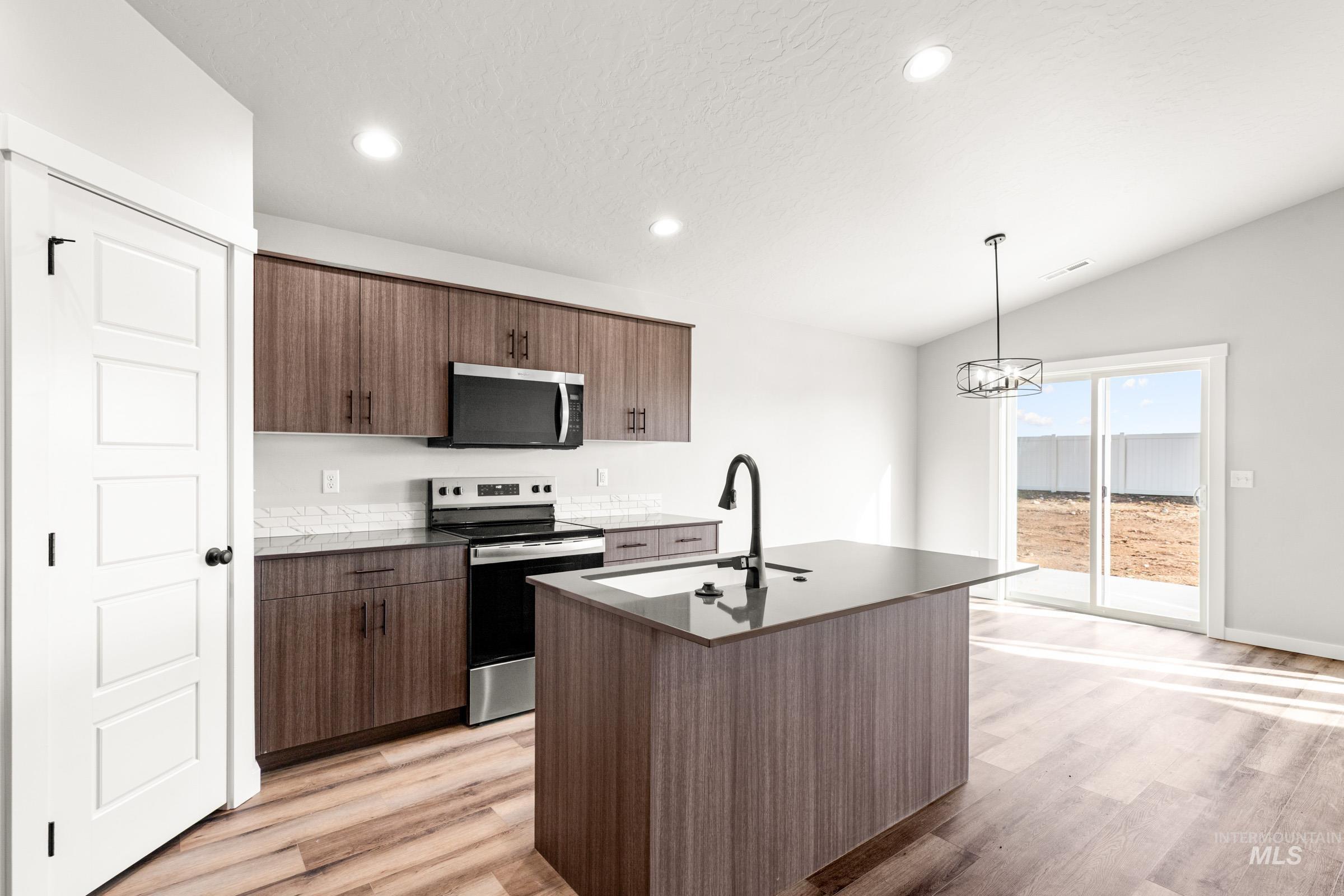 Kitchen featuring stainless steel appliances, light wood-type flooring, a kitchen island with sink, lofted ceiling, and dark wood finish cabinets