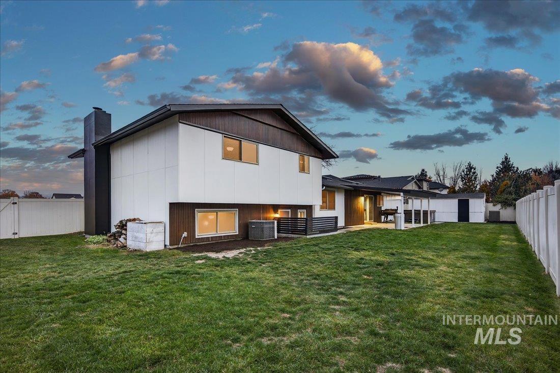 Back of house at dusk featuring a fenced backyard, a chimney, and a patio