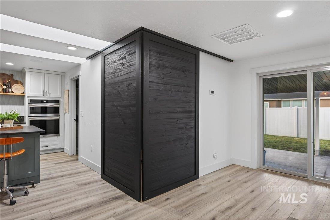 Kitchen featuring recessed lighting, gray cabinetry, stainless steel double oven, light wood-type flooring, and open shelves