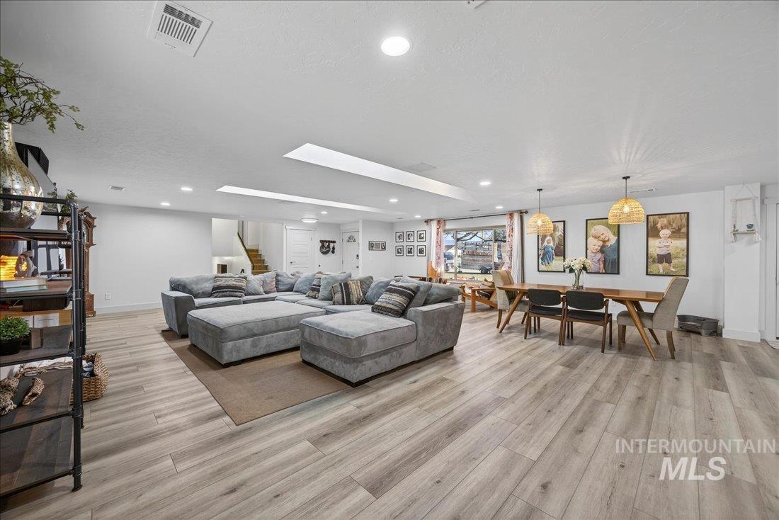 Living room with recessed lighting, light wood-style flooring, stairs, a textured ceiling, and a skylight