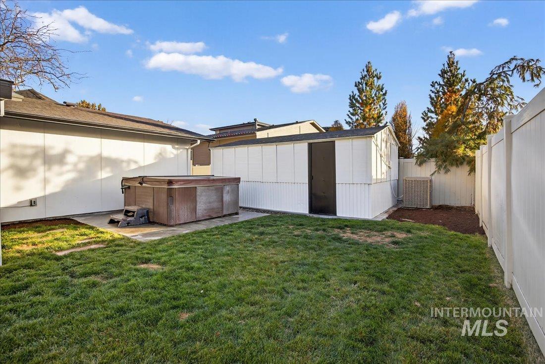 Fenced backyard featuring a hot tub and a storage shed