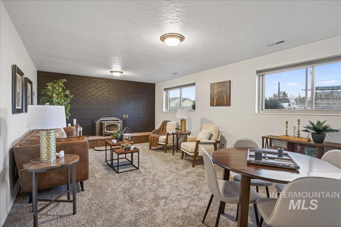 Living room featuring a wood stove, healthy amount of natural light, brick wall, light colored carpet, and a textured ceiling