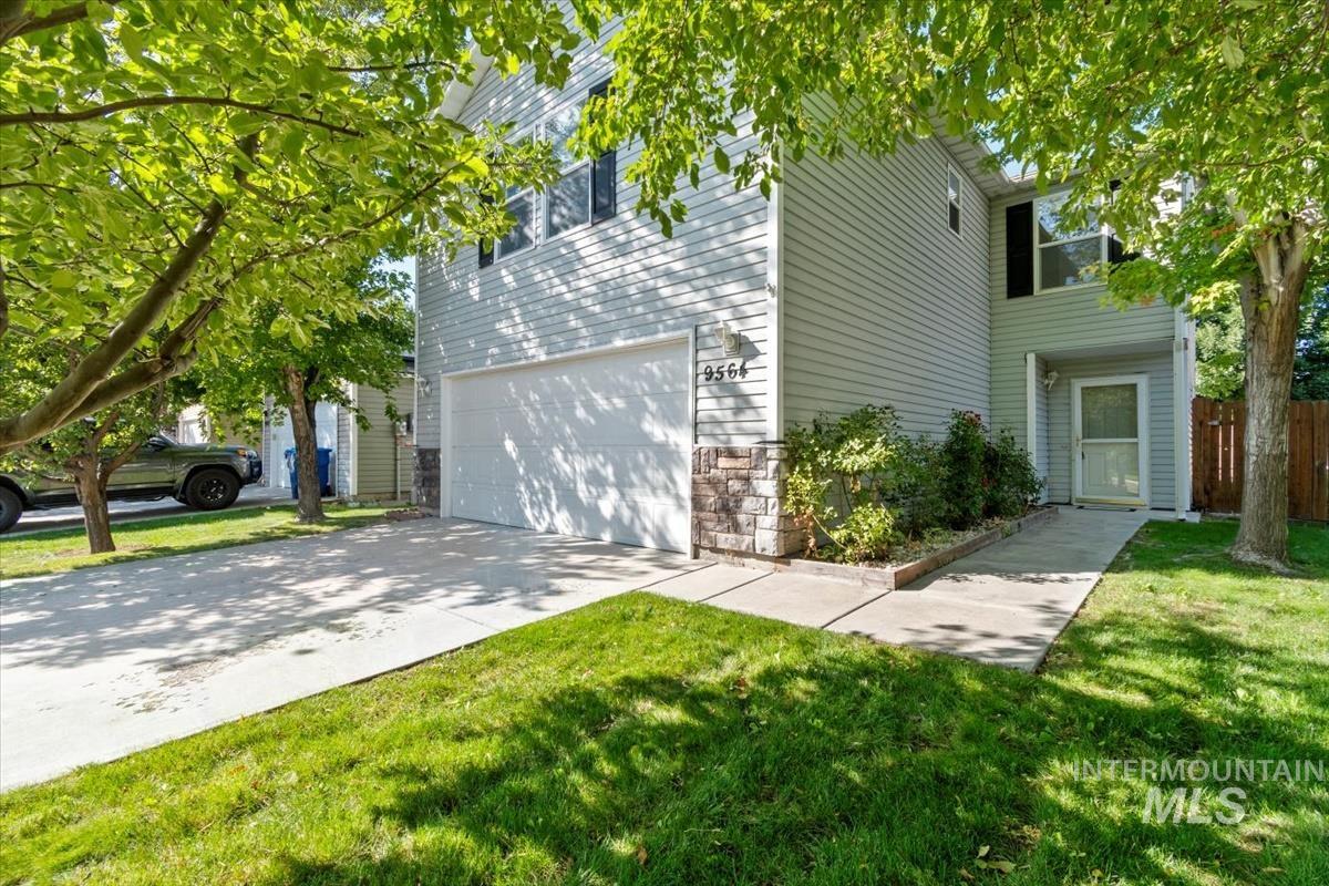 View of front of property with an attached garage, concrete driveway, stone siding, and a front yard