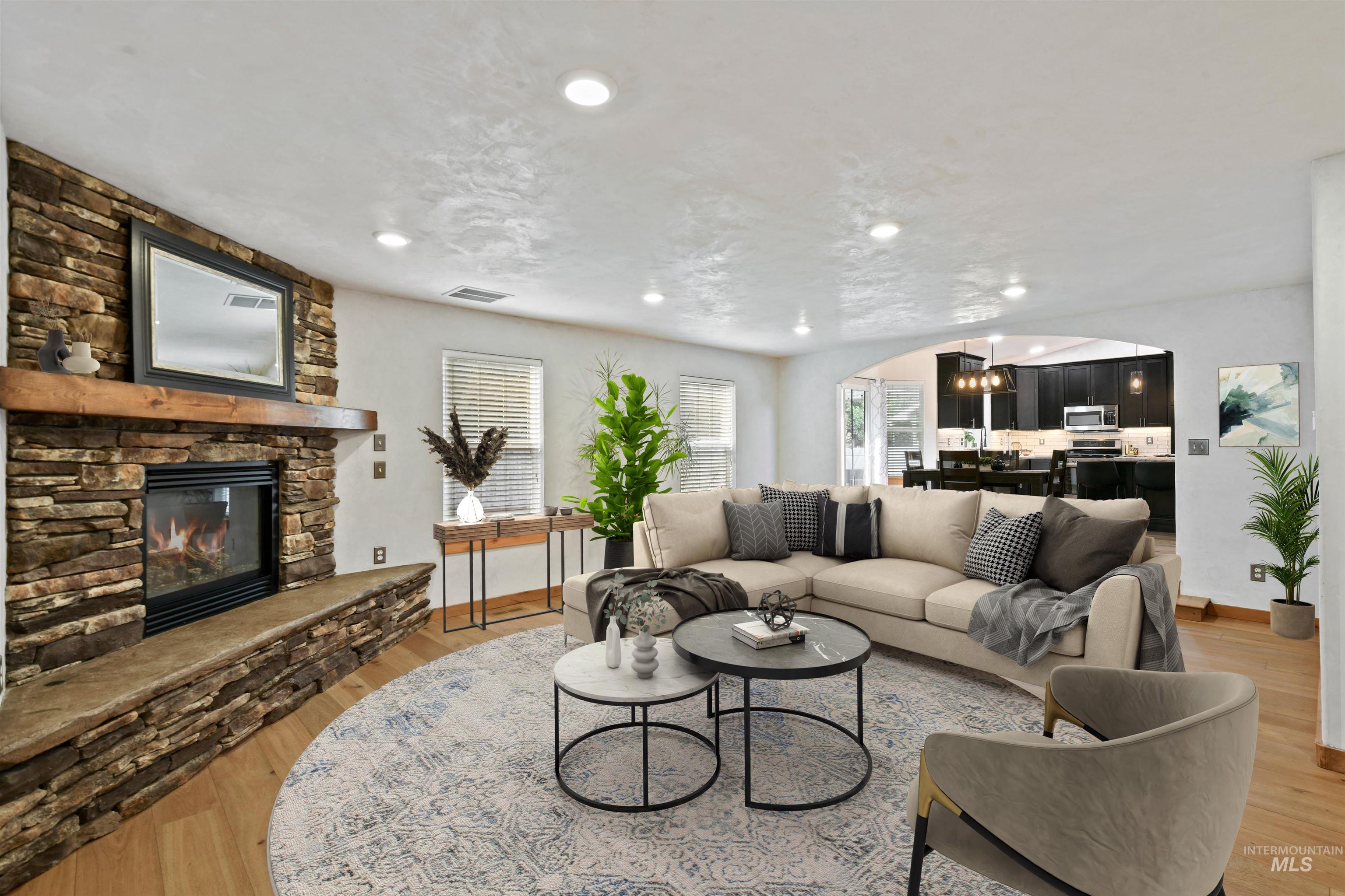 Great room features arched entry with stone gas fireplace, hardwood floors, and recessed lighting.