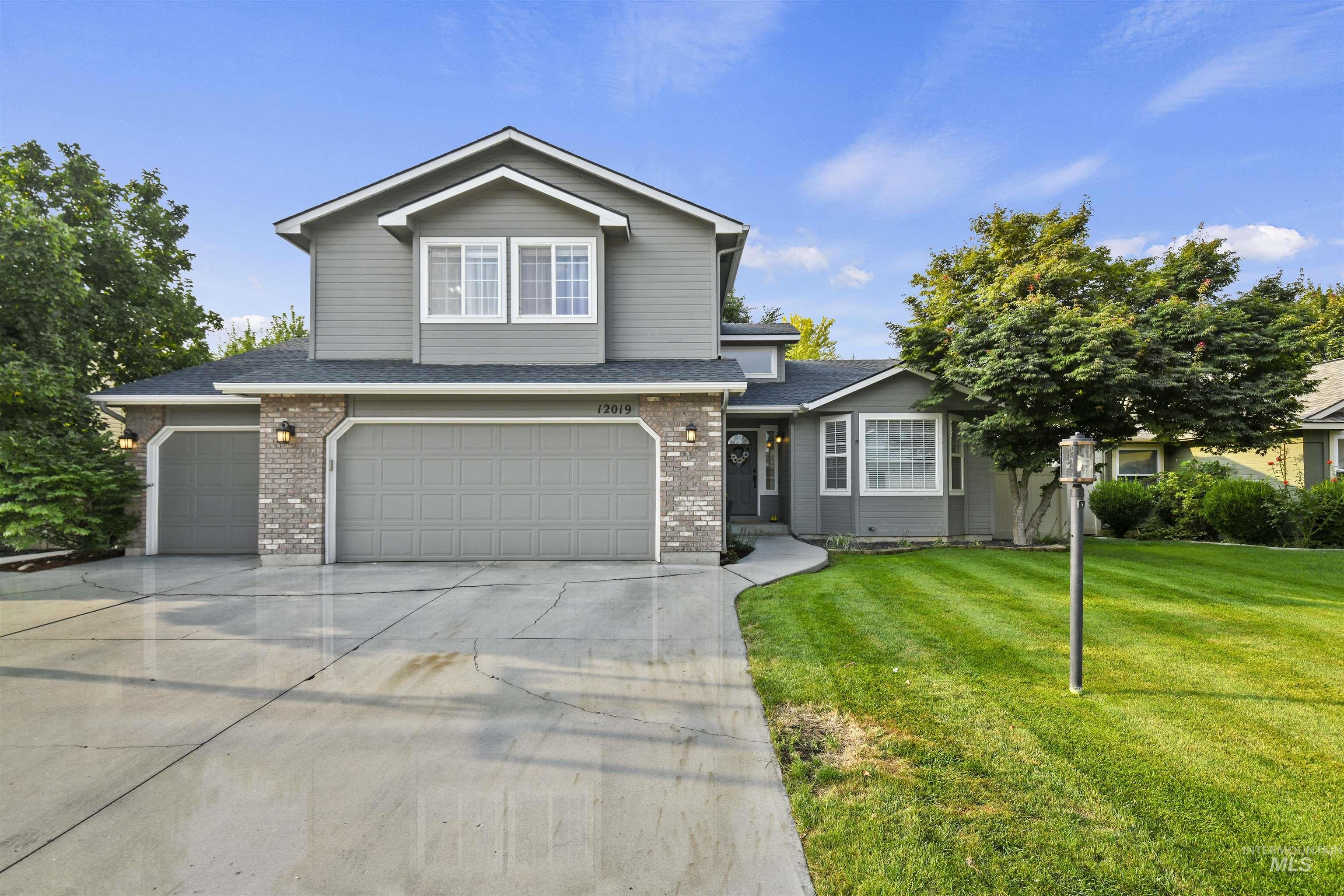 Traditional-style house with driveway, a garage, a front lawn, roof with shingles, and brick siding