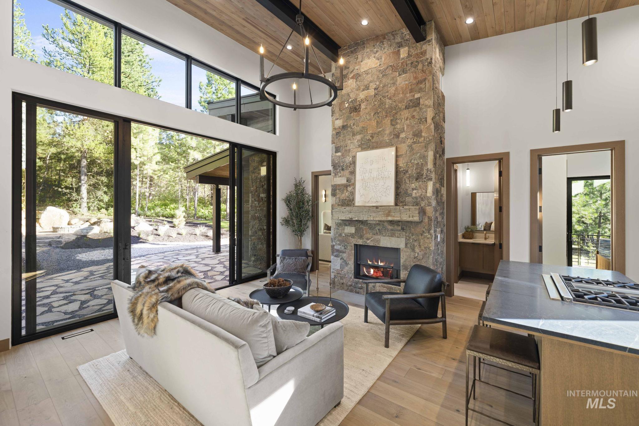 Living area featuring light wood finished floors, a towering ceiling, a wood ceiling with exposed beams, a fireplace, and a chandelier