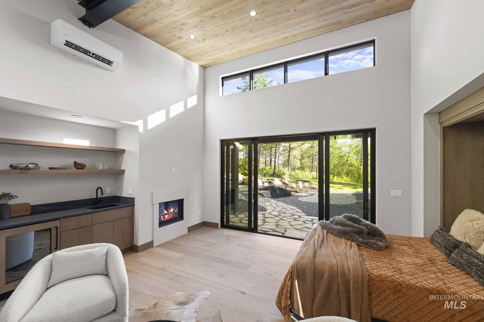 Foyer entrance featuring wood ceiling, light wood-style flooring, a high ceiling, a wall mounted air conditioner, and a glass covered fireplace