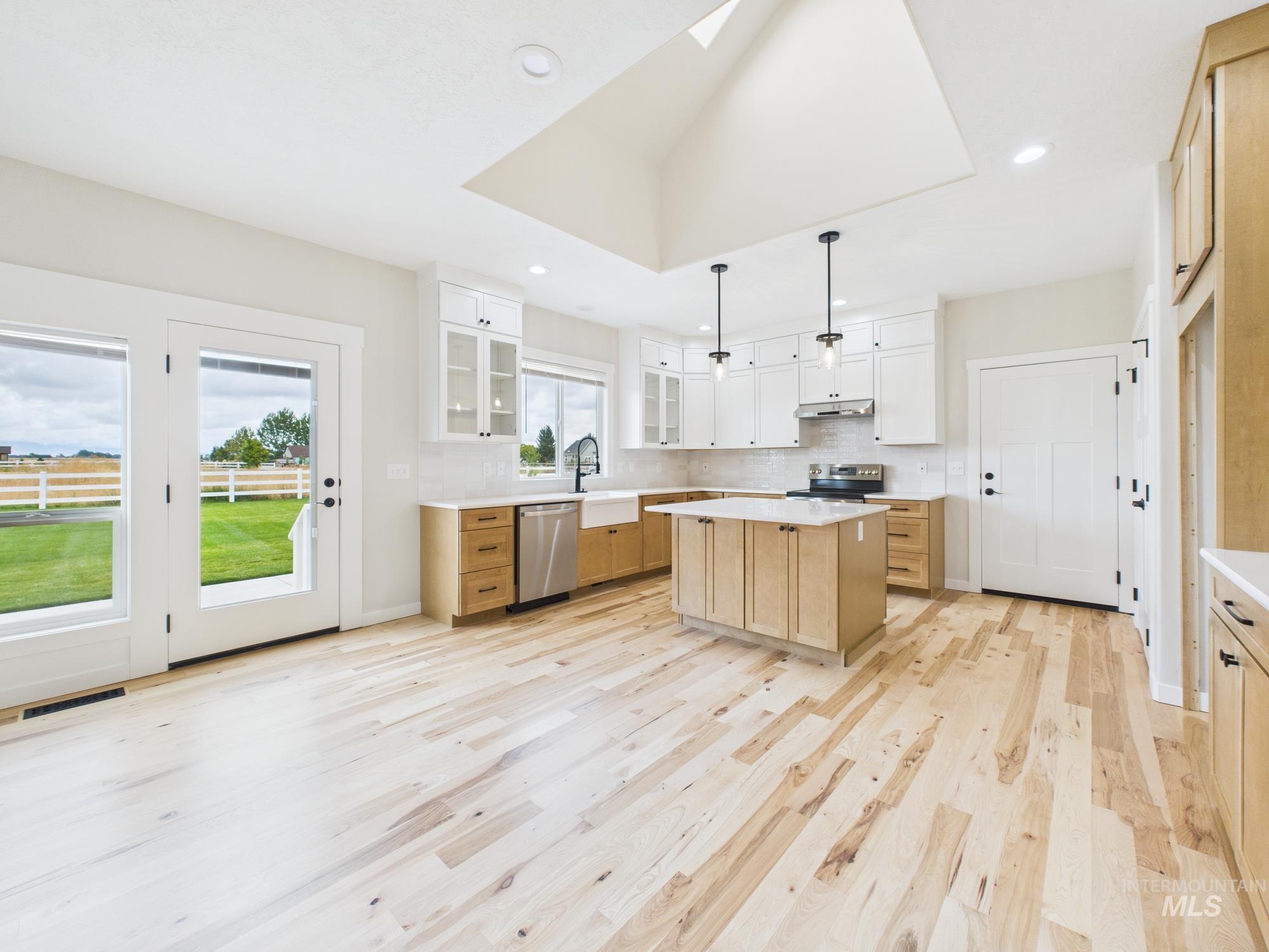 Kitchen featuring backsplash, light brown cabinetry, glass insert cabinets, hanging light fixtures, and light wood finished floors