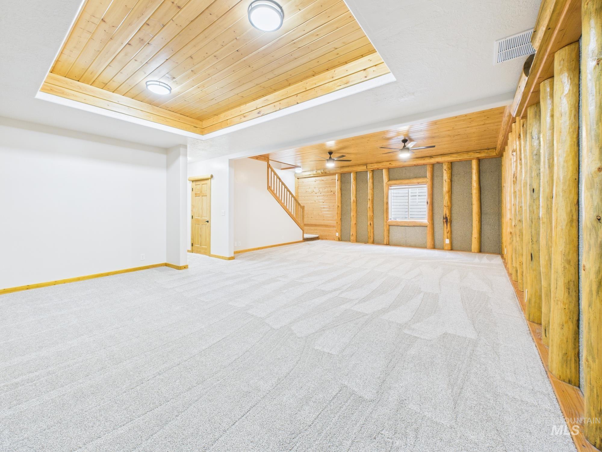 Unfurnished living room with wooden ceiling, a tray ceiling, light colored carpet, and stairway