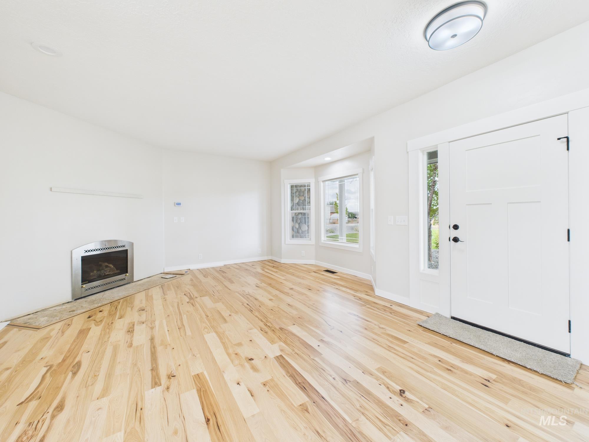 Unfurnished living room with a glass covered fireplace and light wood-style floors
