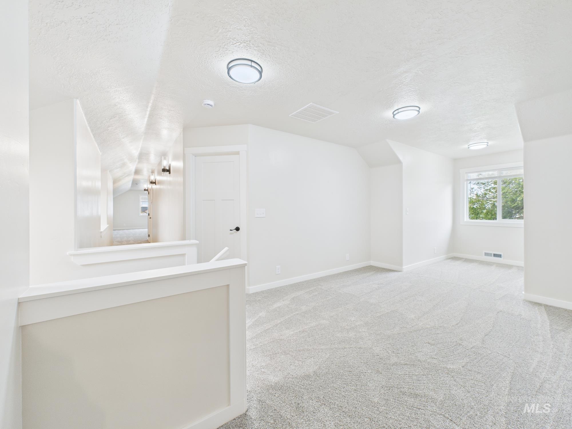 Additional living space with light carpet, a textured ceiling, and vaulted ceiling