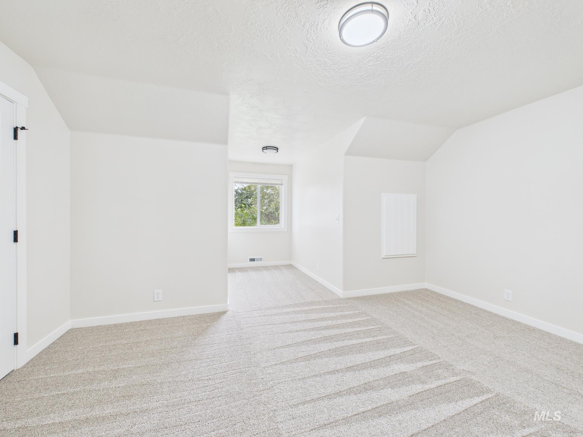 Unfurnished room featuring light colored carpet, lofted ceiling, and a textured ceiling