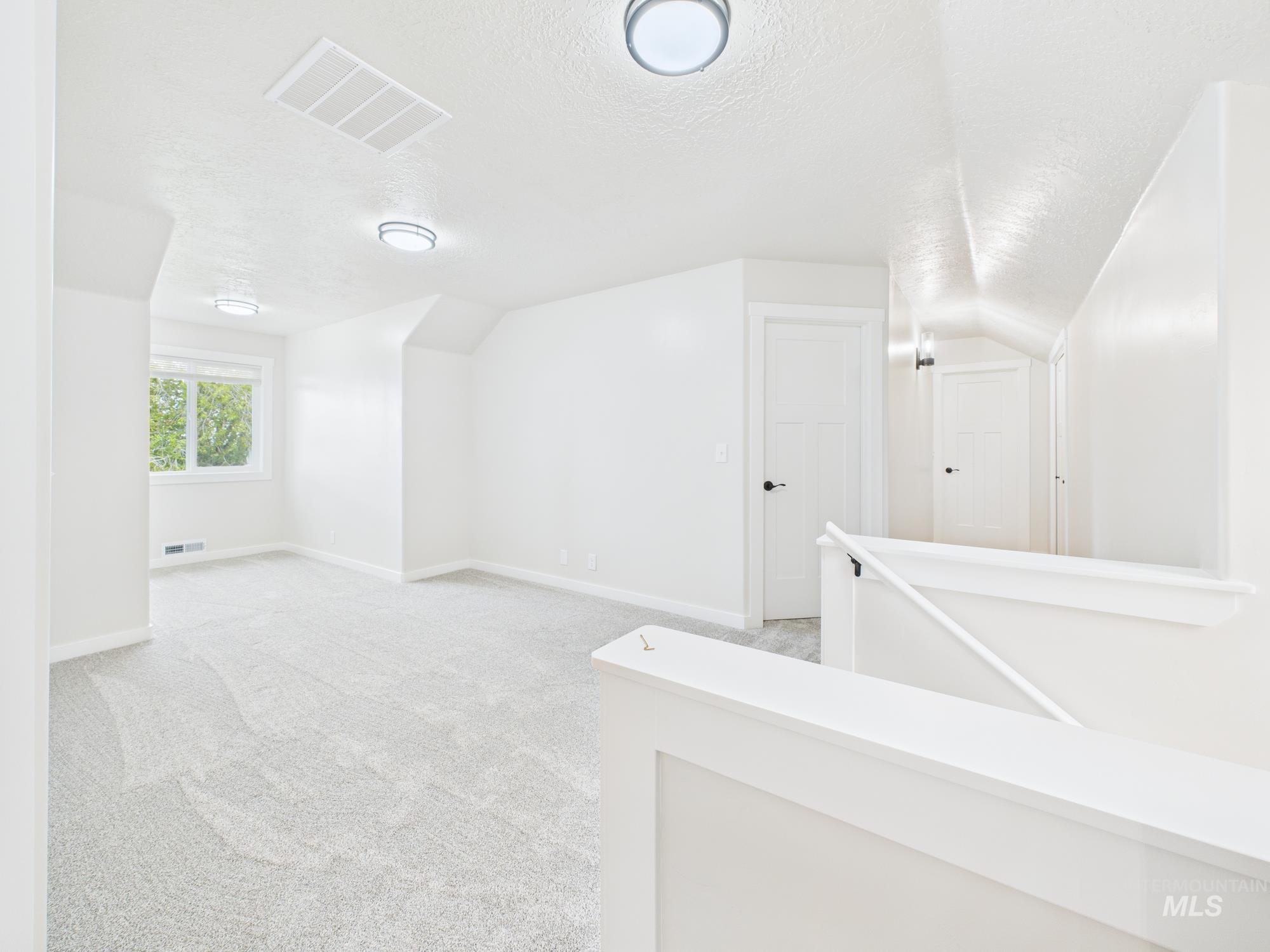 Bonus room with a textured ceiling, light carpet, and vaulted ceiling