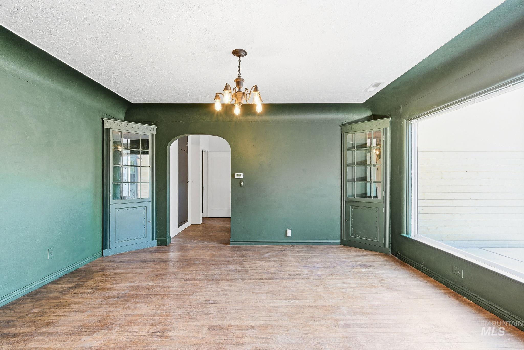 Unfurnished dining area featuring arched walkways, suspended lighting, and wood finished floors