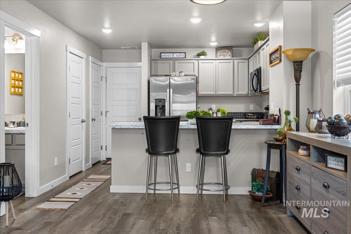 Kitchen featuring gray cabinets, stainless steel fridge with ice dispenser, dark wood-style flooring, a peninsula, and a kitchen bar
