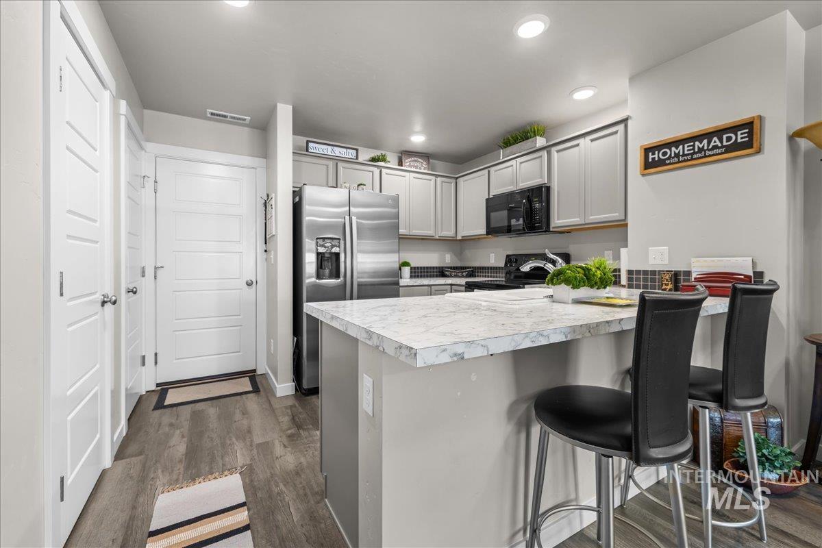 Kitchen featuring dark wood-style flooring, light countertops, gray cabinets, black appliances, and a kitchen breakfast bar