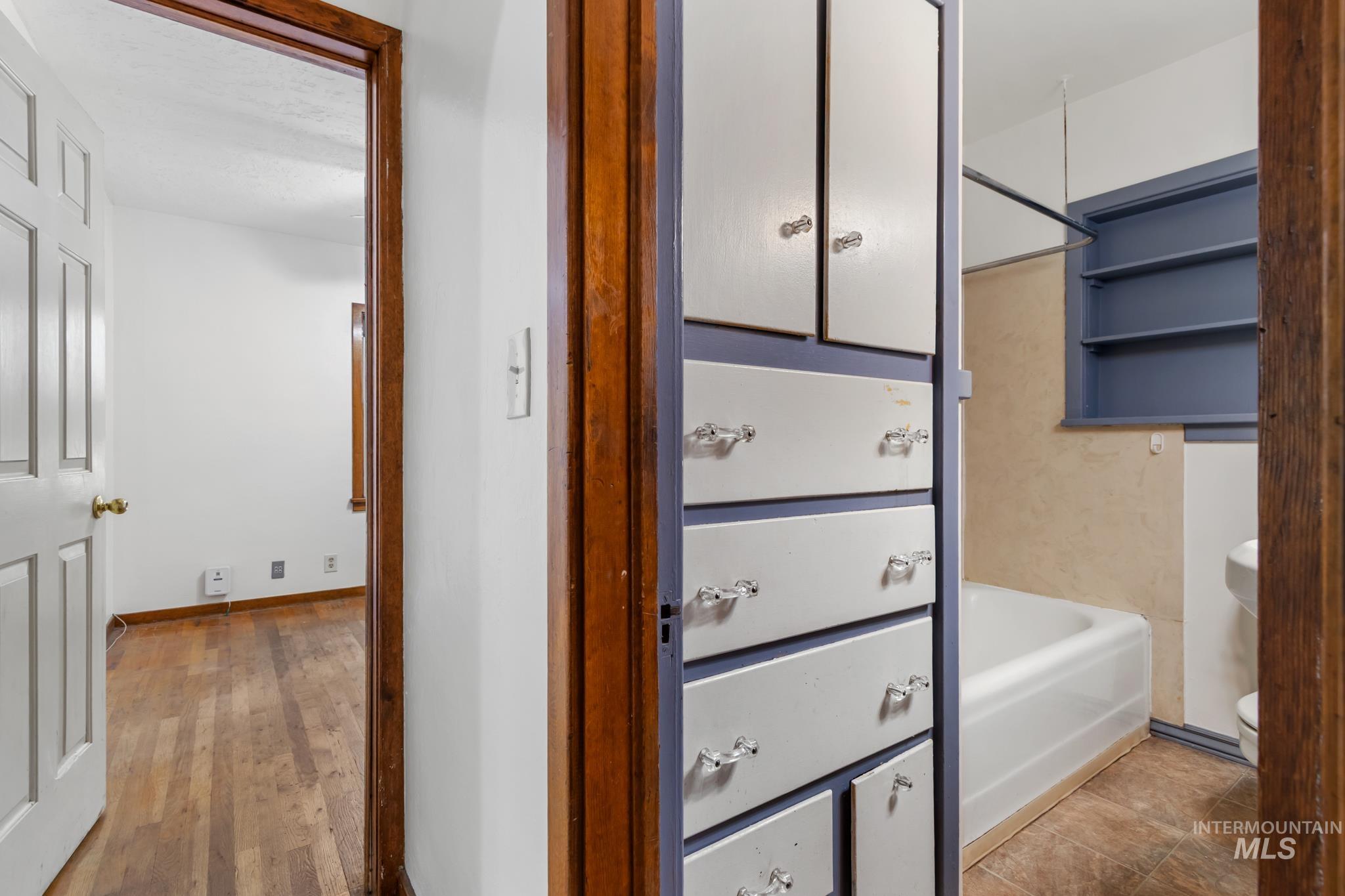 Built-in storage cabinet with multiple drawers and upper cabinets, full bathtub with shower rod, recessed wall shelving, and a pedestal sink