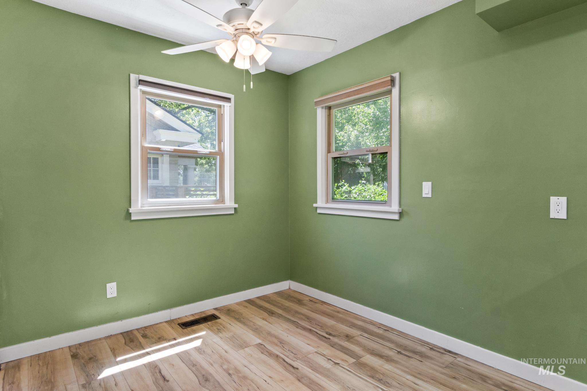Room with wood-finish flooring, two windows, and a ceiling fan