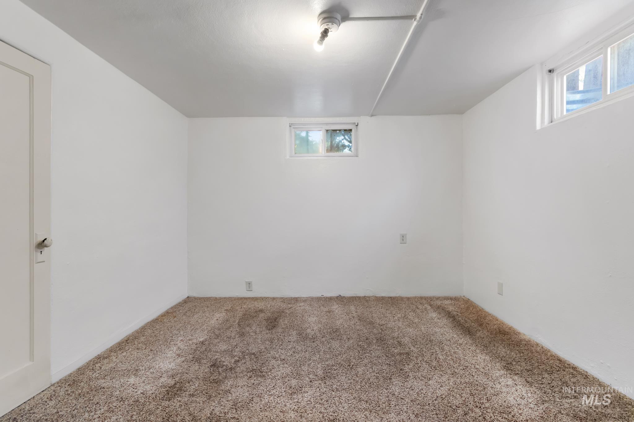 Spacious room featuring neutral carpeting, white painted walls, and overhead lighting
