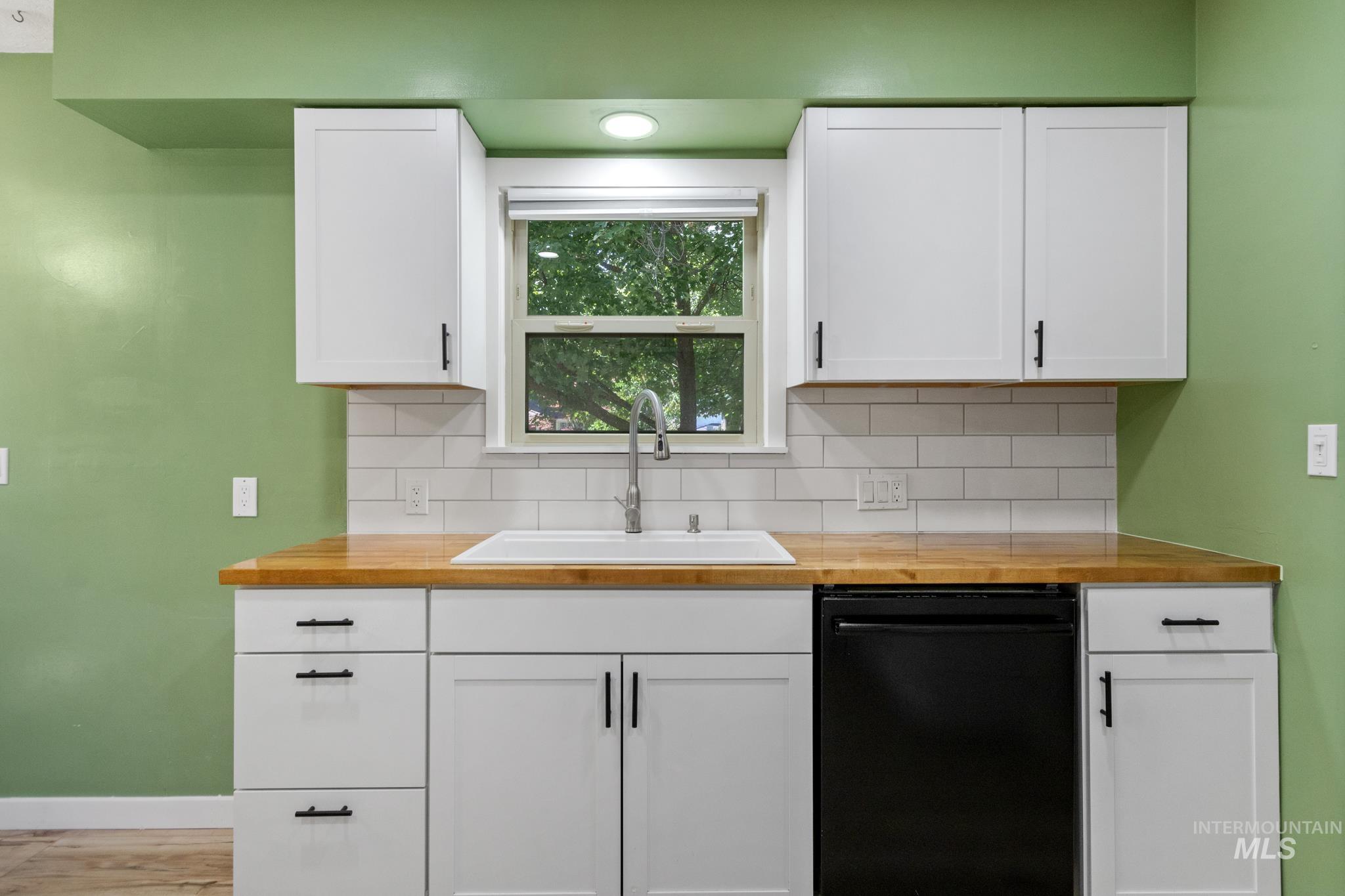 Kitchen featuring a white undermount sink, a black dishwasher, and white shaker-style cabinetry with black hardware