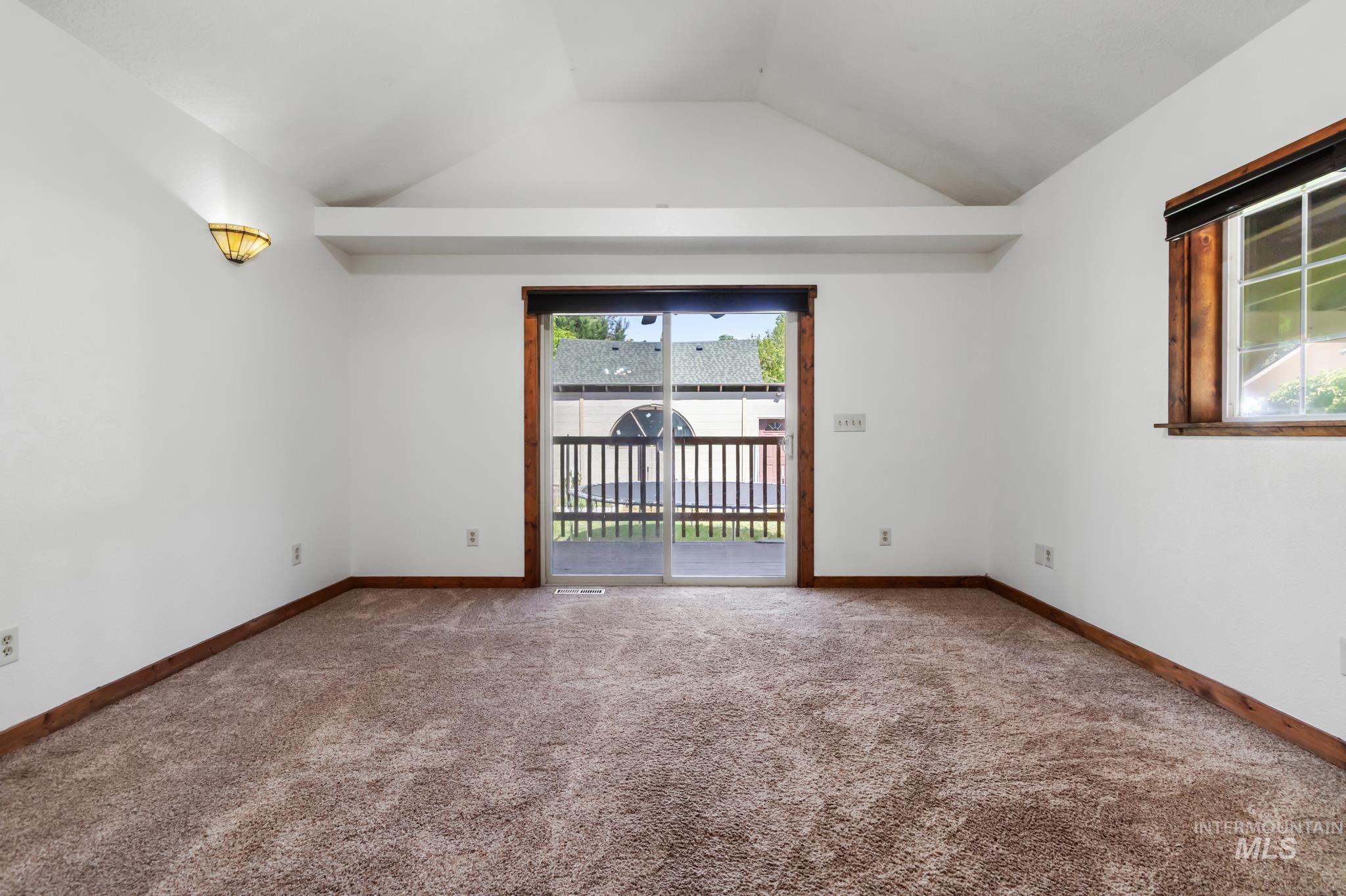 Carpeted interior space featuring a vaulted ceiling and a glass sliding door providing outdoor access