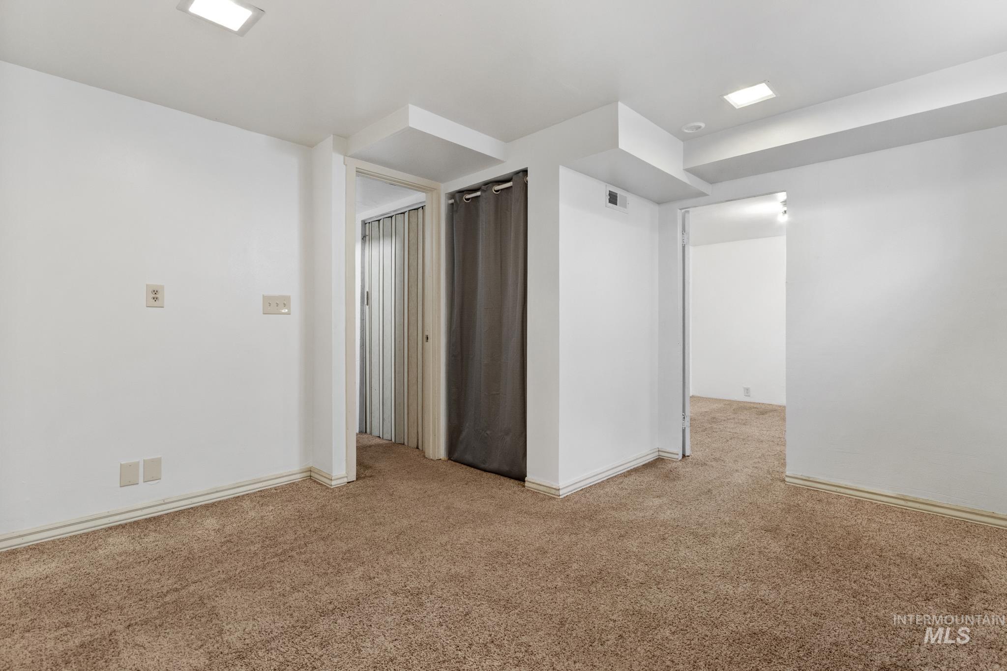 Spacious room featuring neutral carpeting, white walls, recessed ceiling lighting, and multiple entryways with trim detailing