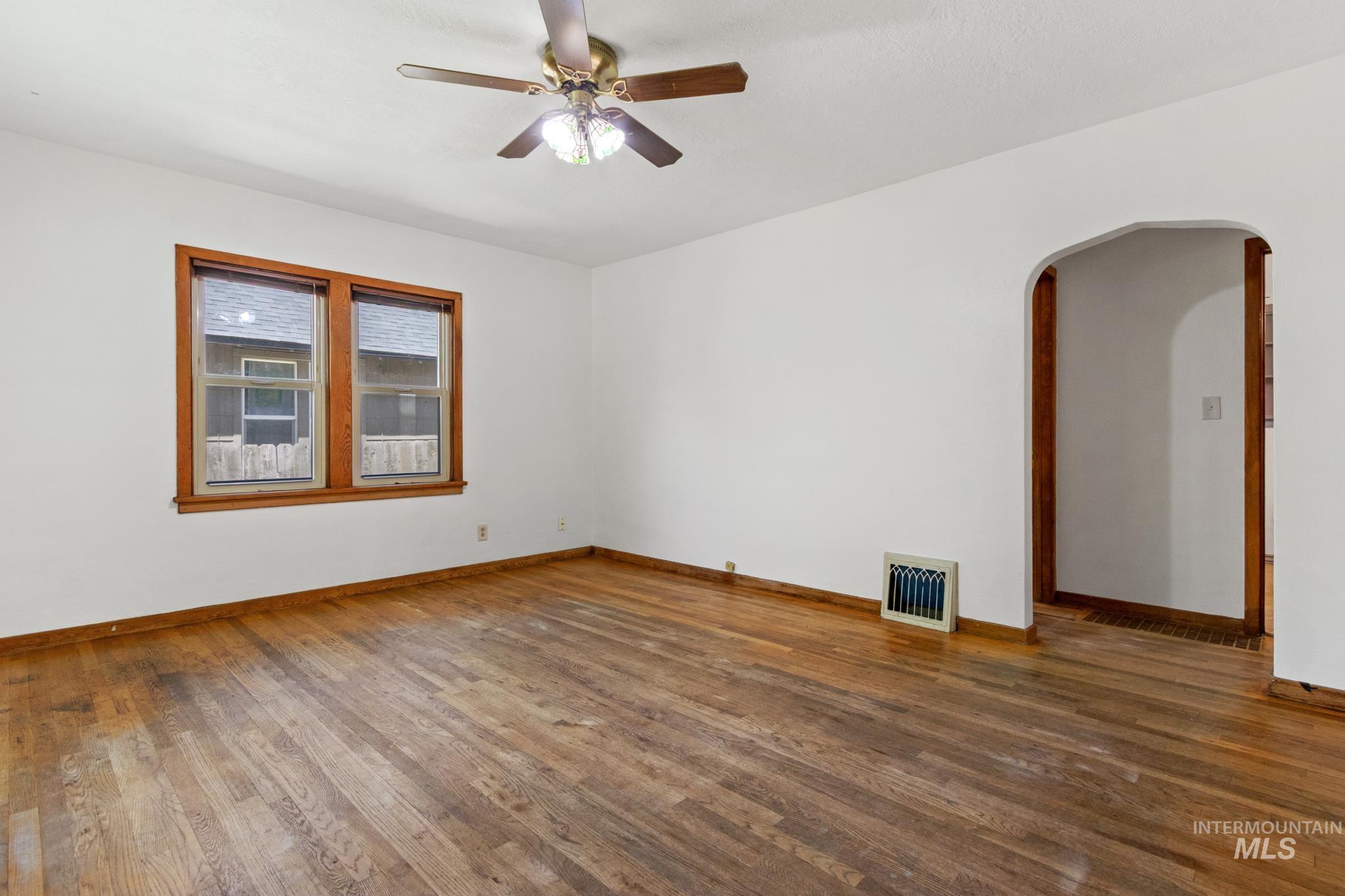 Spacious room featuring wood-finish flooring, white walls, and a ceiling fan