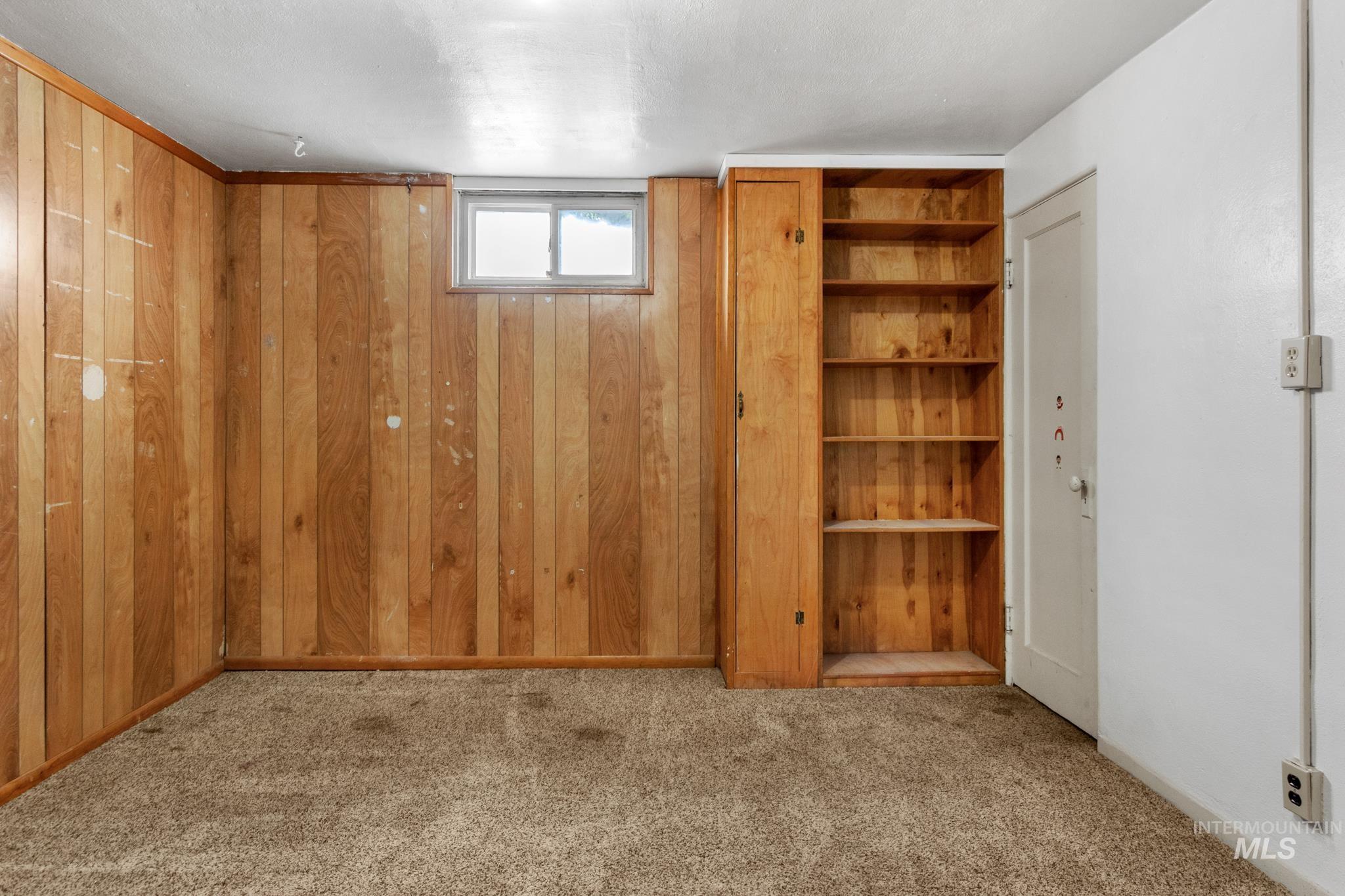 Room featuring light wood paneling, a small window, built-in wooden shelving, and a neutral carpet