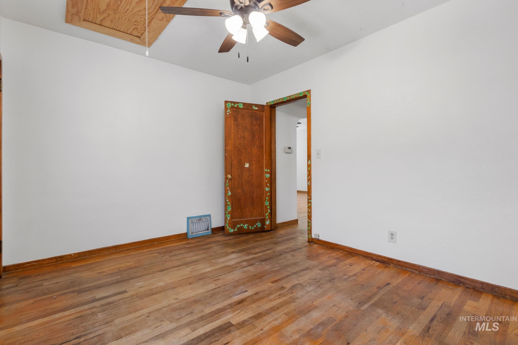Spacious room with light wood-finish flooring, white walls, and dark wood trim